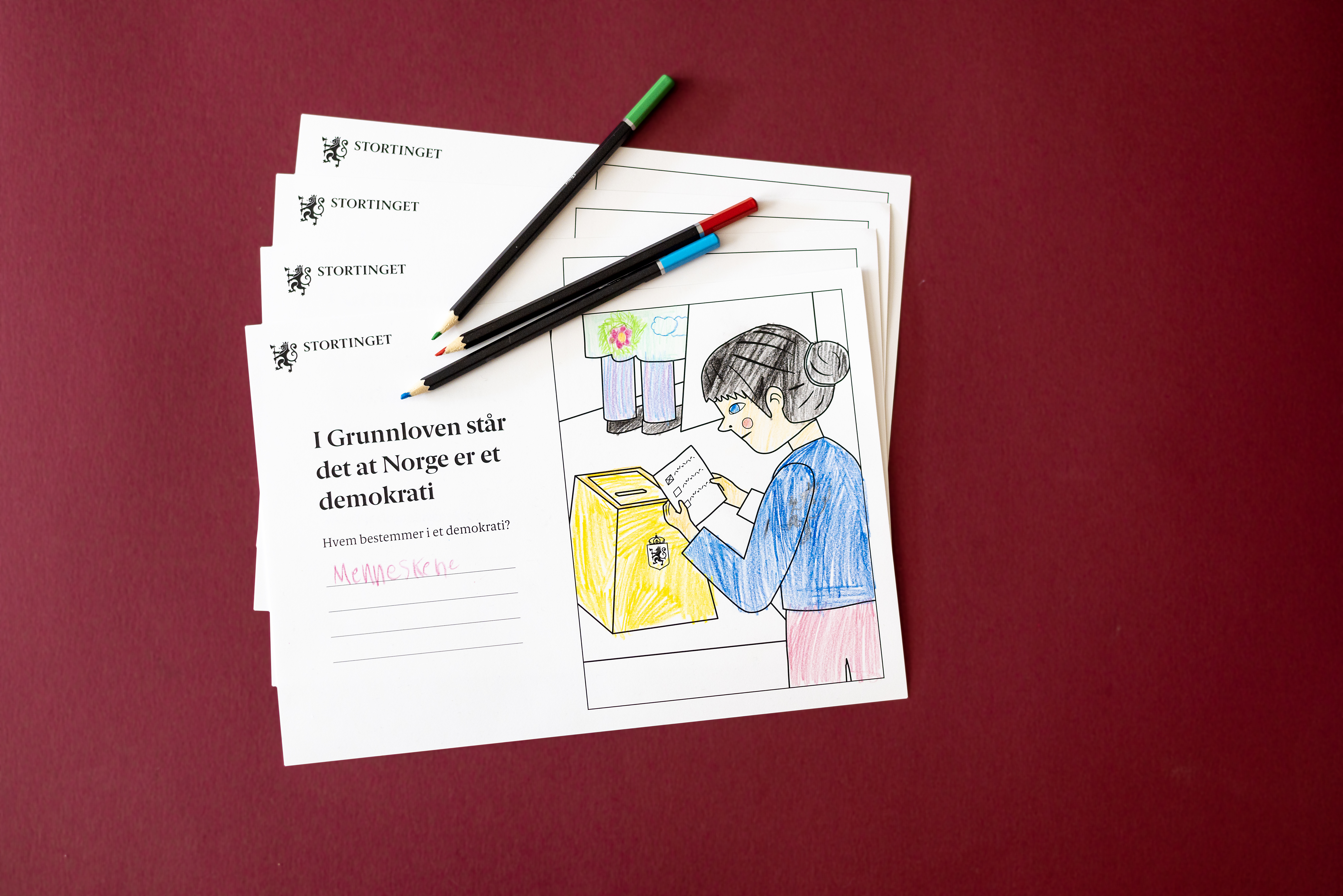 Ark fra oppgavehefte ligger oppå hverandre, med noen blyanter på toppen. 