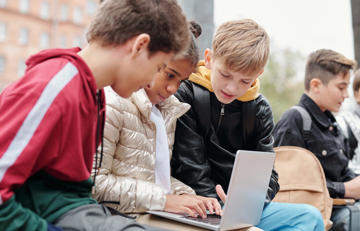 Tre ungdommer sitter ved siden av hverandre og ser på skjermen på en laptop.