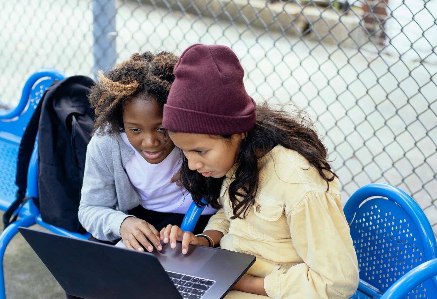 To jenter sitter på en benk med en laptop på fanget.