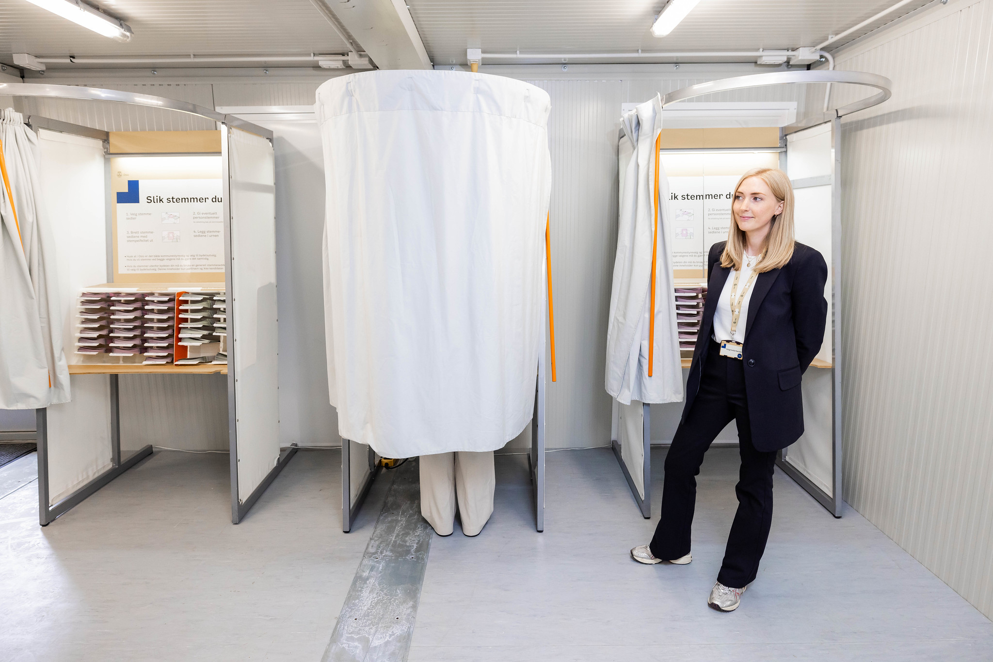 Person står bak forheng i valglokale.