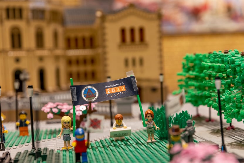Legofigurer holder plakater, med stortingsbygningen i Lego i bakgrunnen.