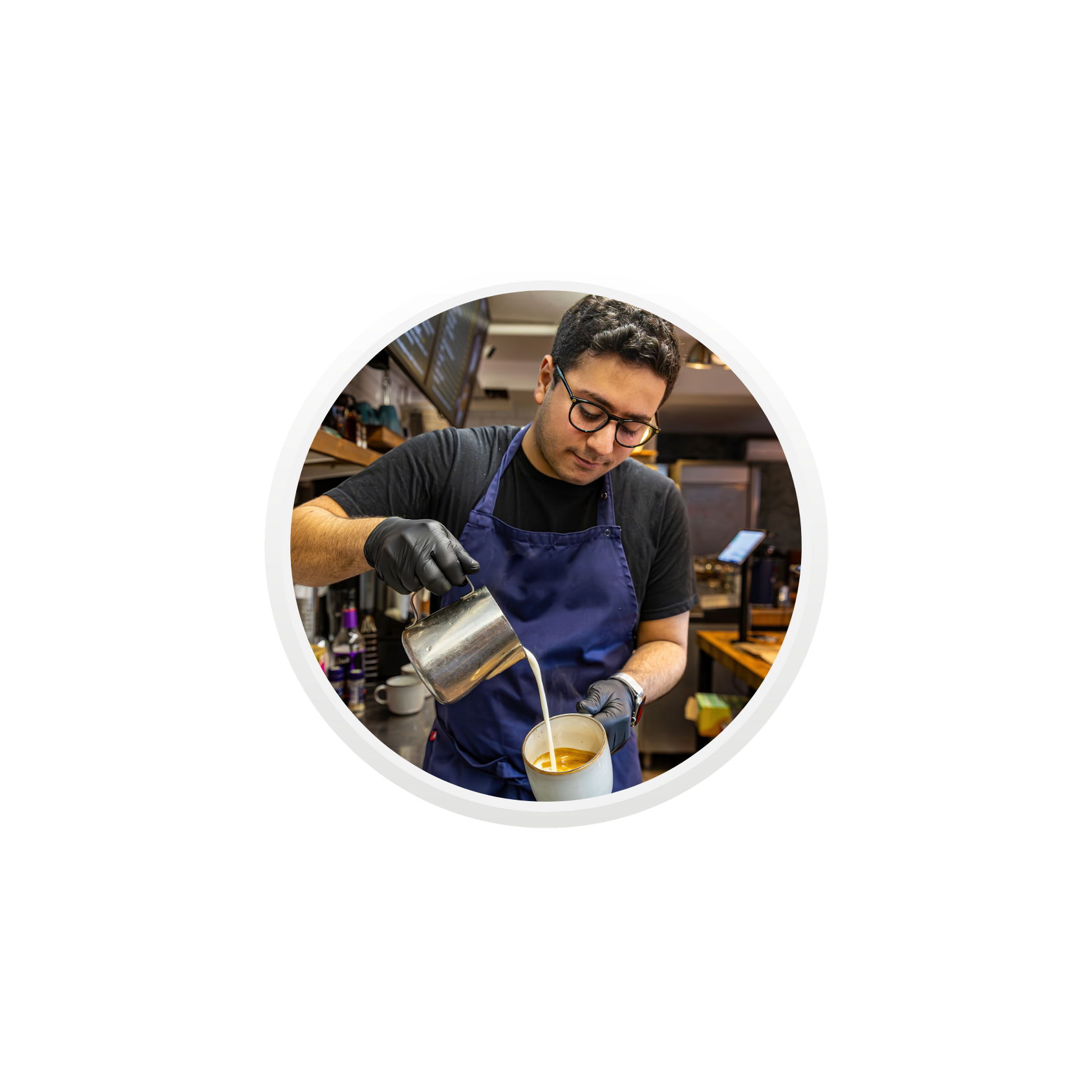 Ung mann som jobber som barista heller steamet melk i en kopp med espresso.