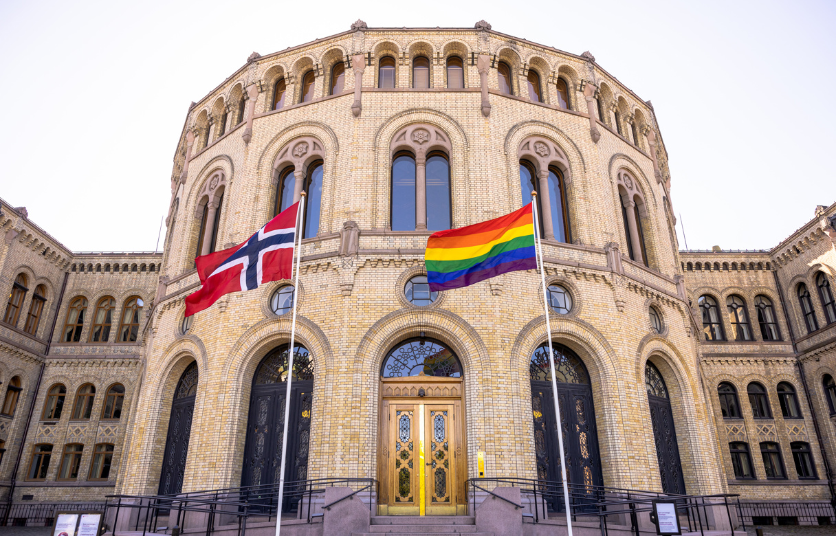 Stortingsbygningen med norsk flagg og regnbueflagg i front