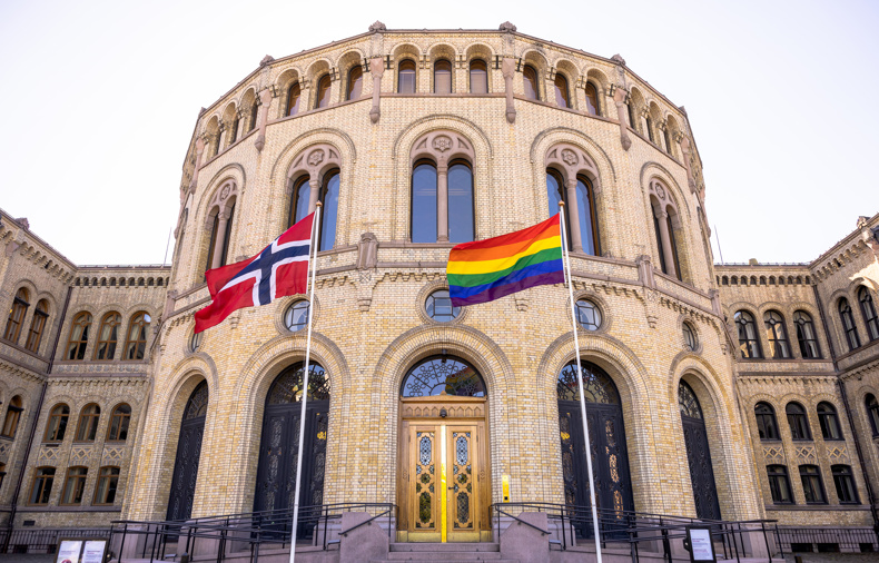 Stortingsbygningen med norsk flagg og regnbueflagg i front