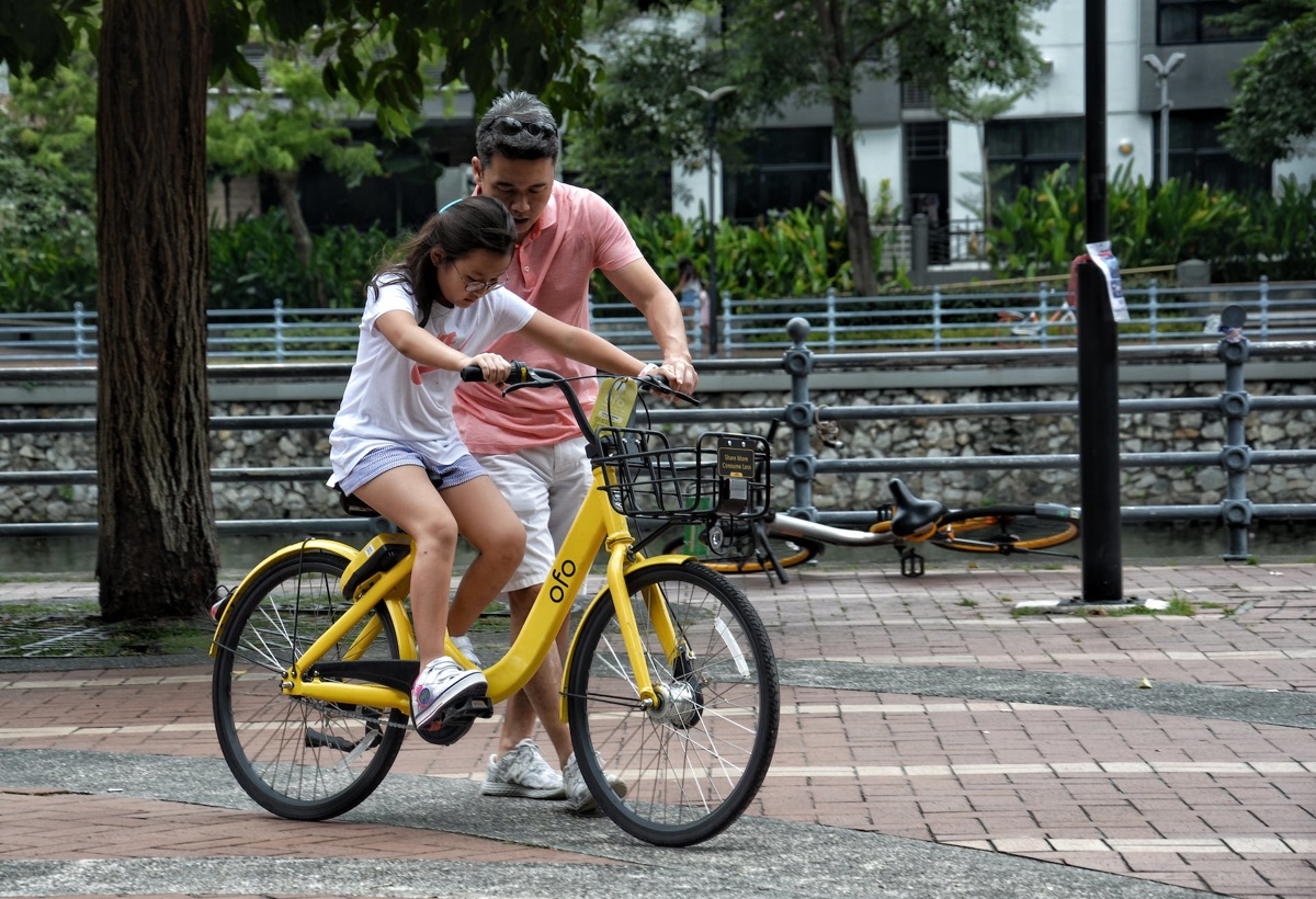 En jente øver seg på å sykle, en mann hjelper henne.