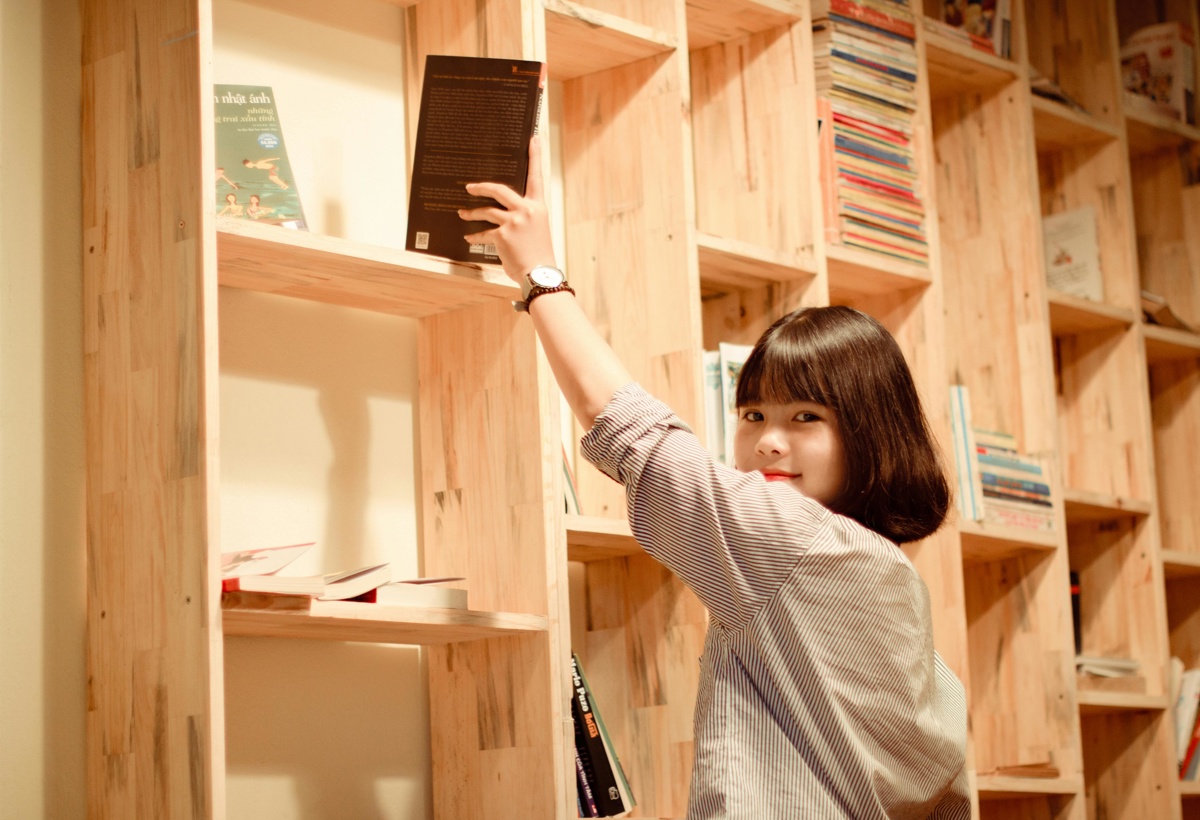 En jente setter en bok inn i en bokhylle.