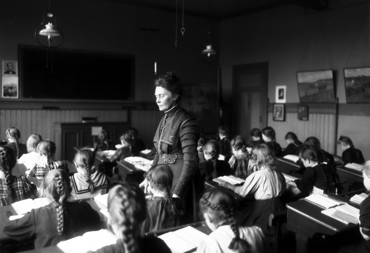 En kvinnelig lærer står midt i et klasserom med bare jenter. Elevene sitter med ryggen mot kamera.