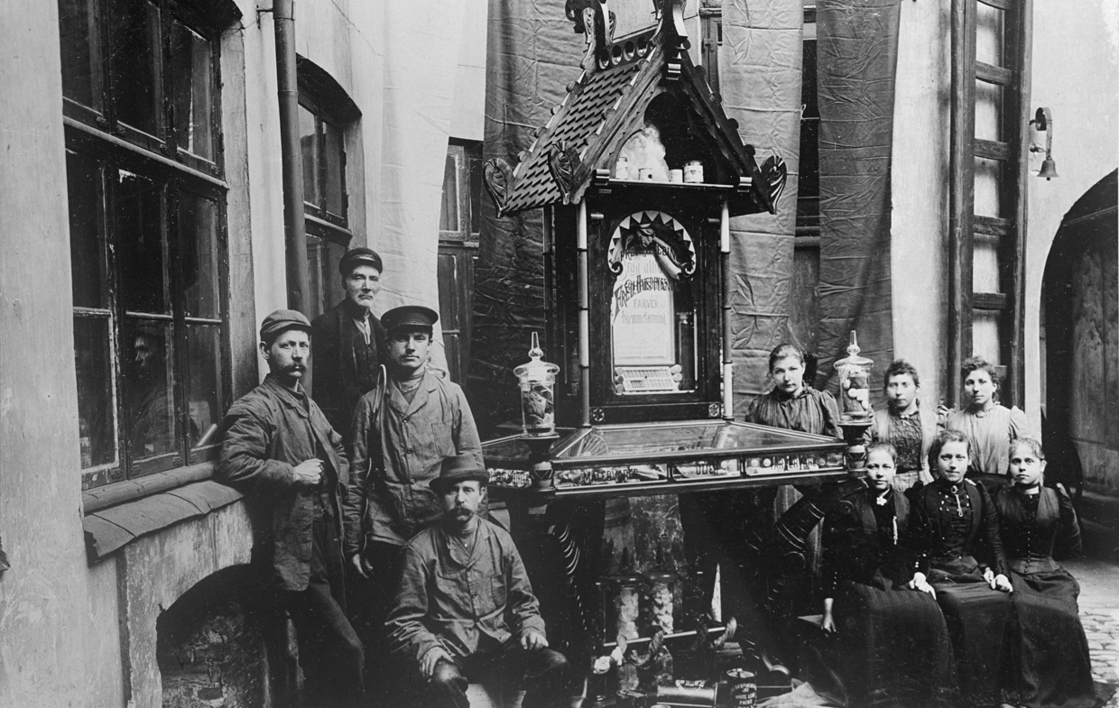 Fire mannlige og seks kvinnelige fabrikkarbeidere sitter foran fabrikken de jobber i.