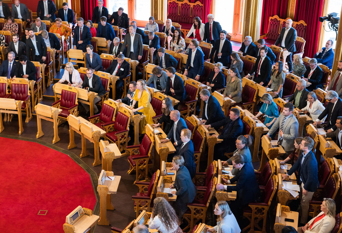 Stortingsrepresentanter i stortingssalen voterer. Noen står og noen sitter.