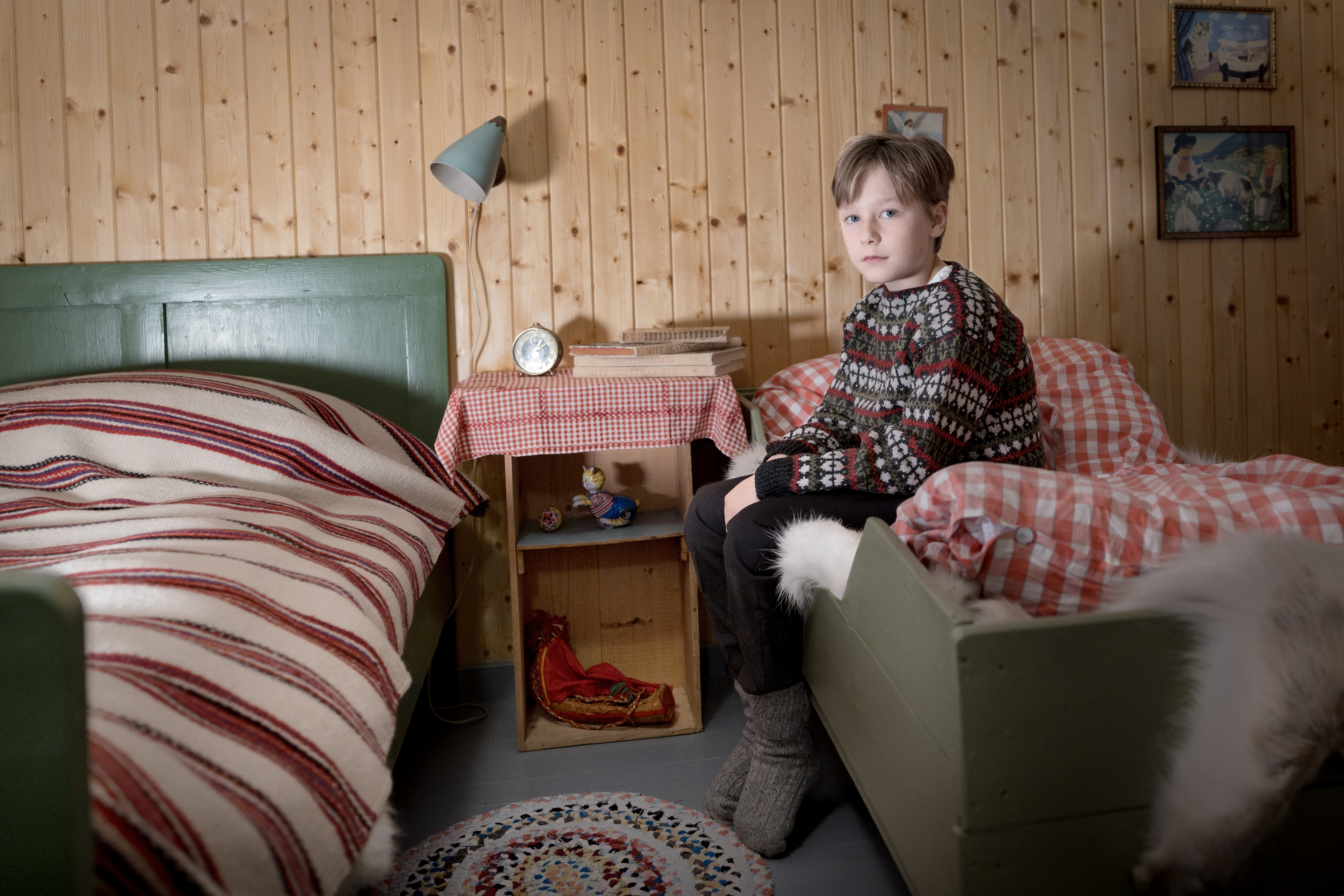 en gutt sitter på en seng, kledd i klær fra 40- tallet