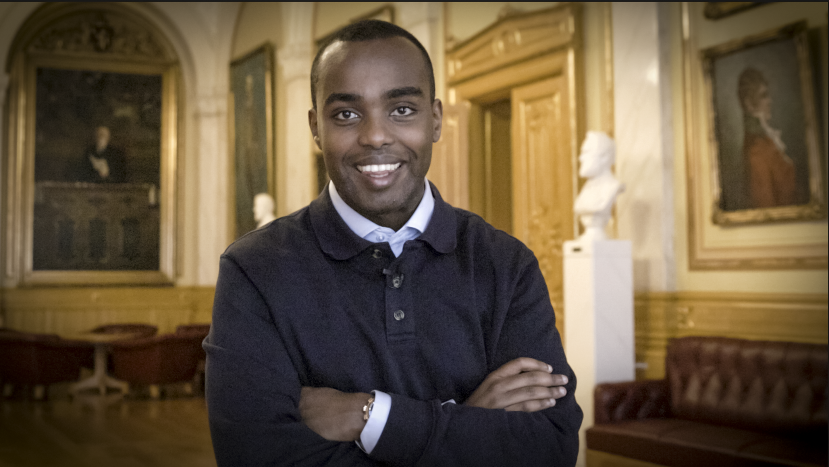 Ung mann ser inn i kamera og smiler, i Eidsvollsgalleriet på Stortinget.