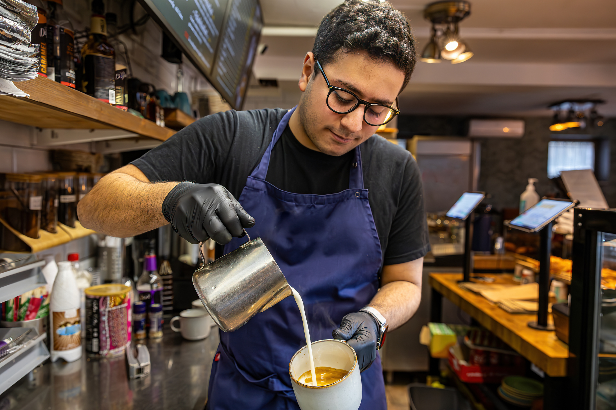 En ung mann som jobber som barista heller steamet melk i en kopp med espresso.