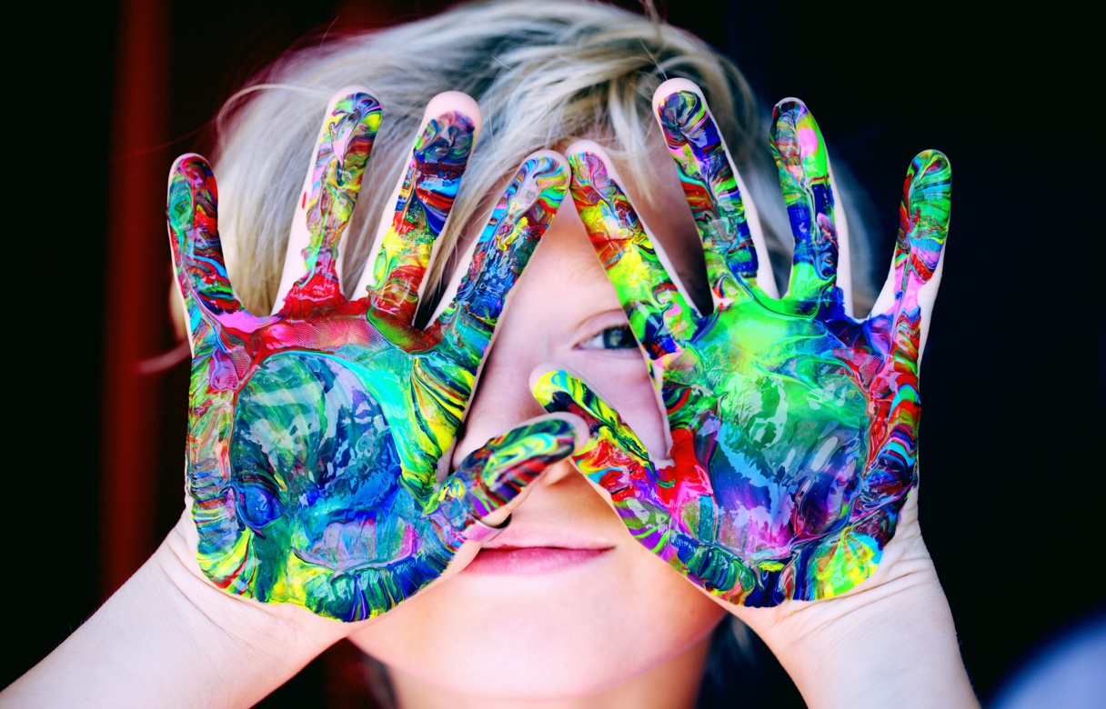Et barn holder hender foran ansiktet. Hendene er malt i luke farger.