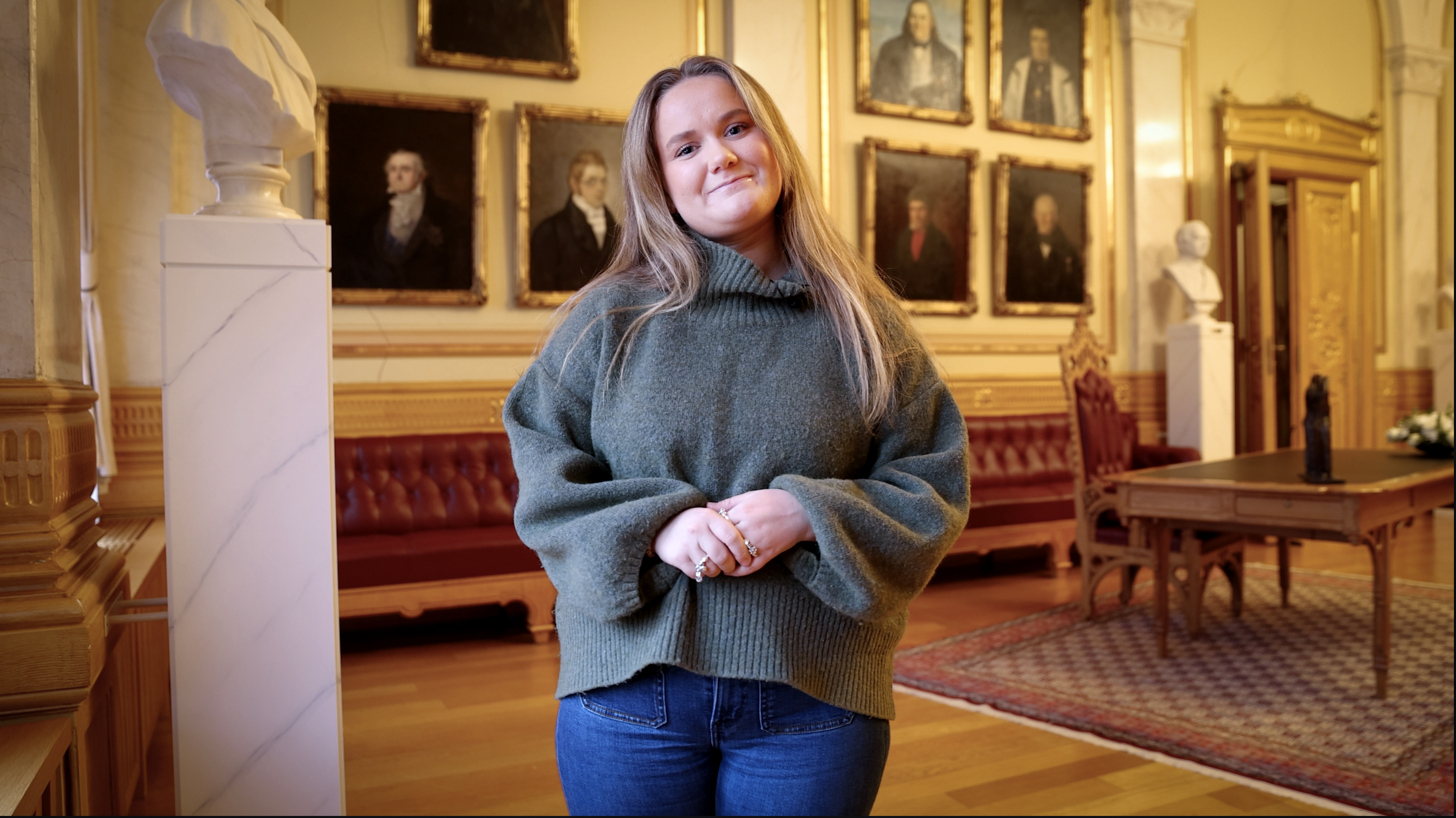 Ung kvinne i Vandrehallen på Stortinget ser mot kamera og smiler.