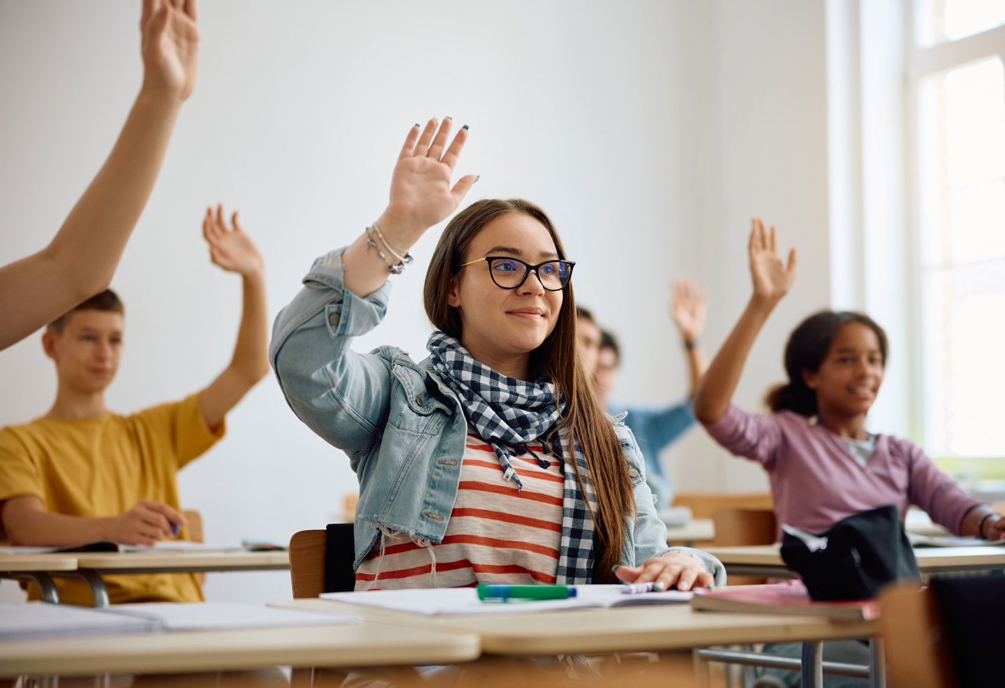 Fem elever i et klasserom. Alle rekker opp hånda.
