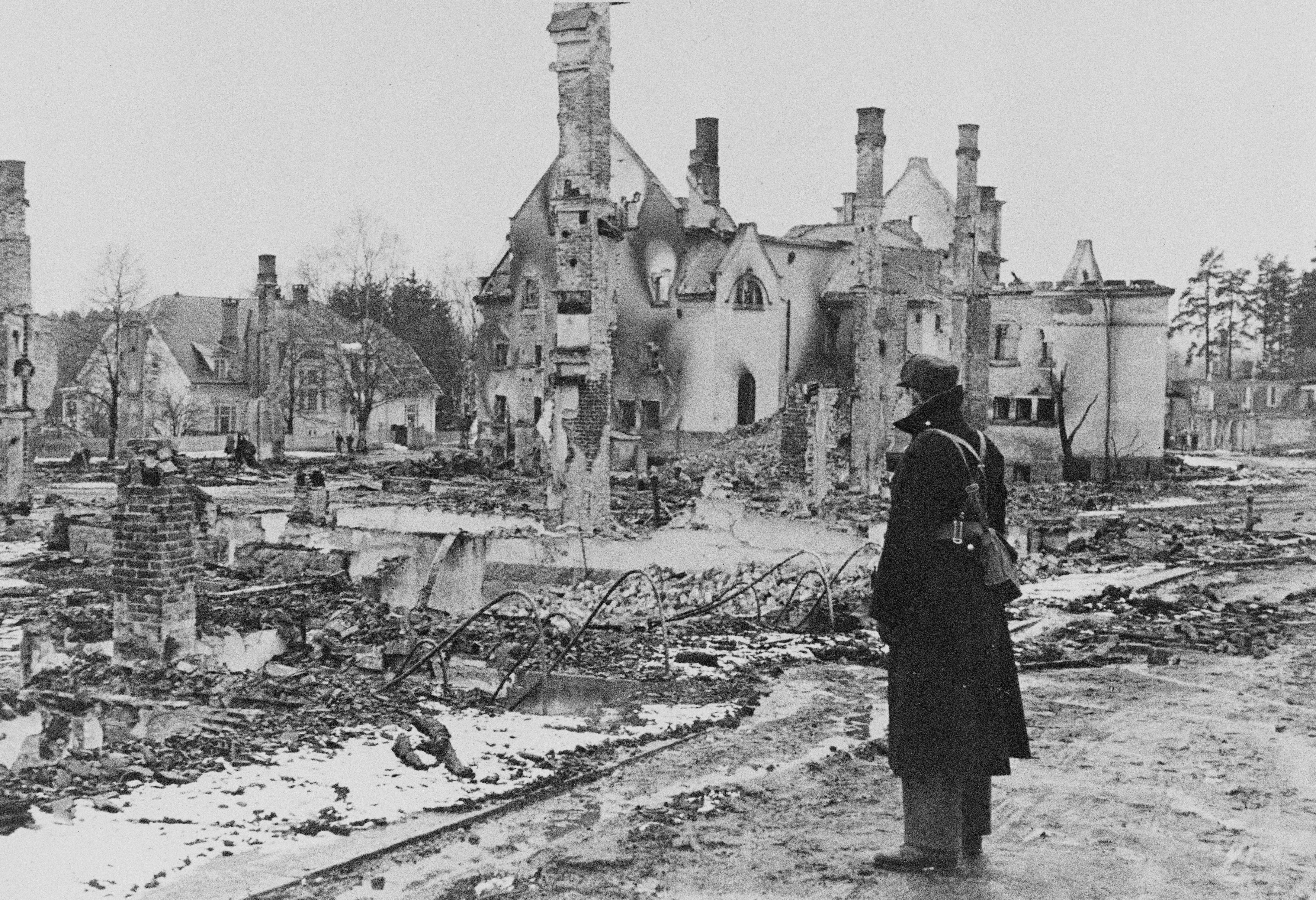 En mann står foran ruinene av flere bygninger.