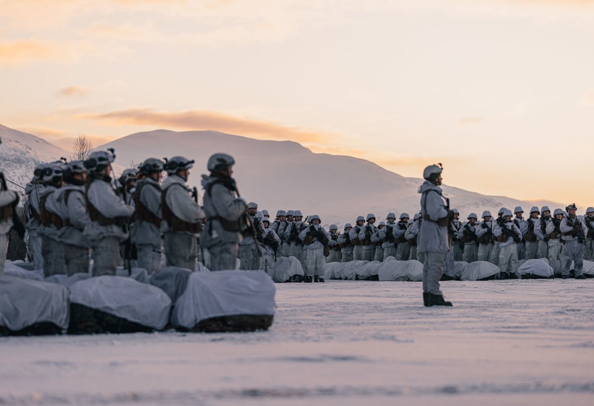 Soldater står i snøen med fjell i bakgrunnen.