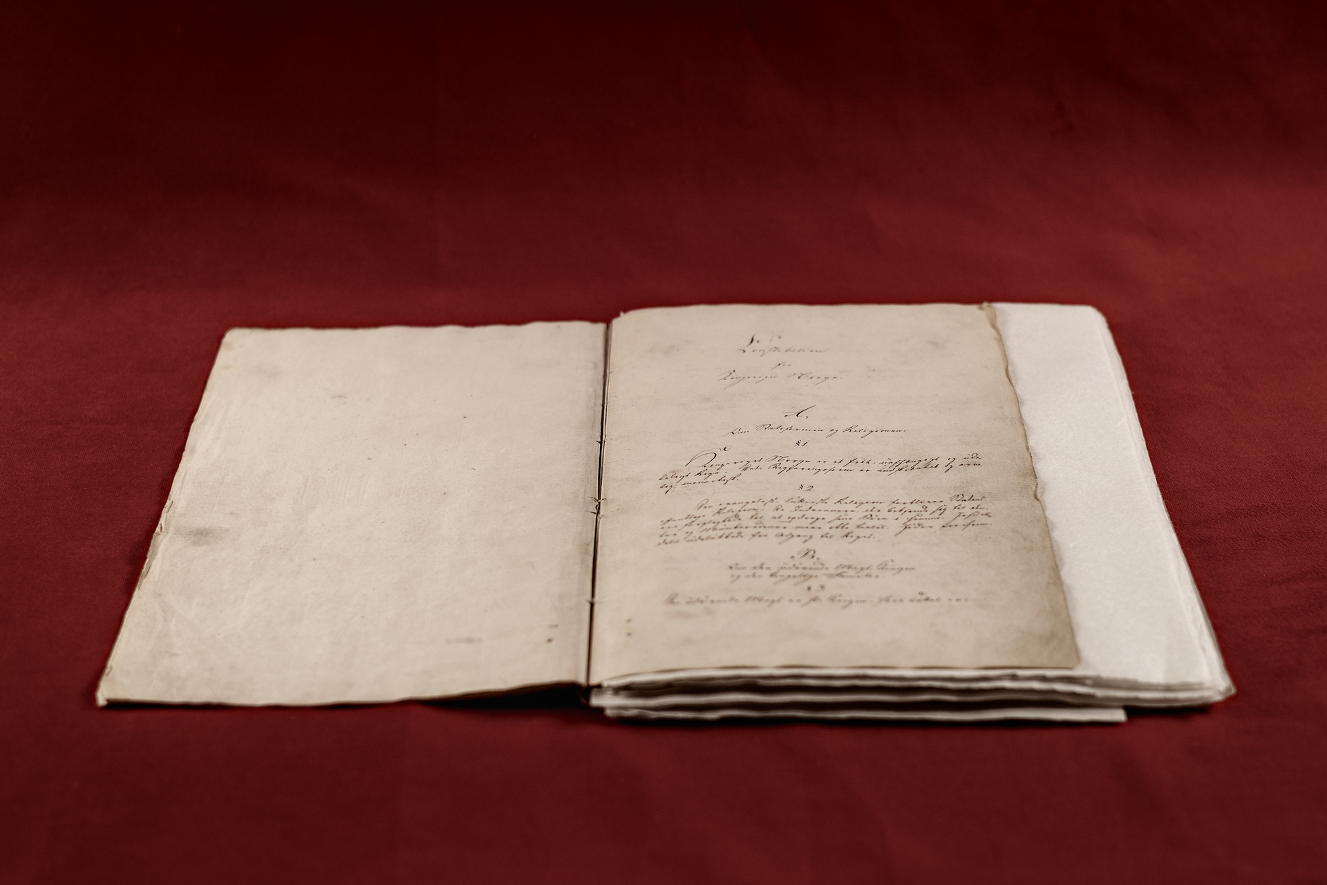 Gammelt dokument med gotisk skrift. Ligger oppslått på et bord med rød duk.