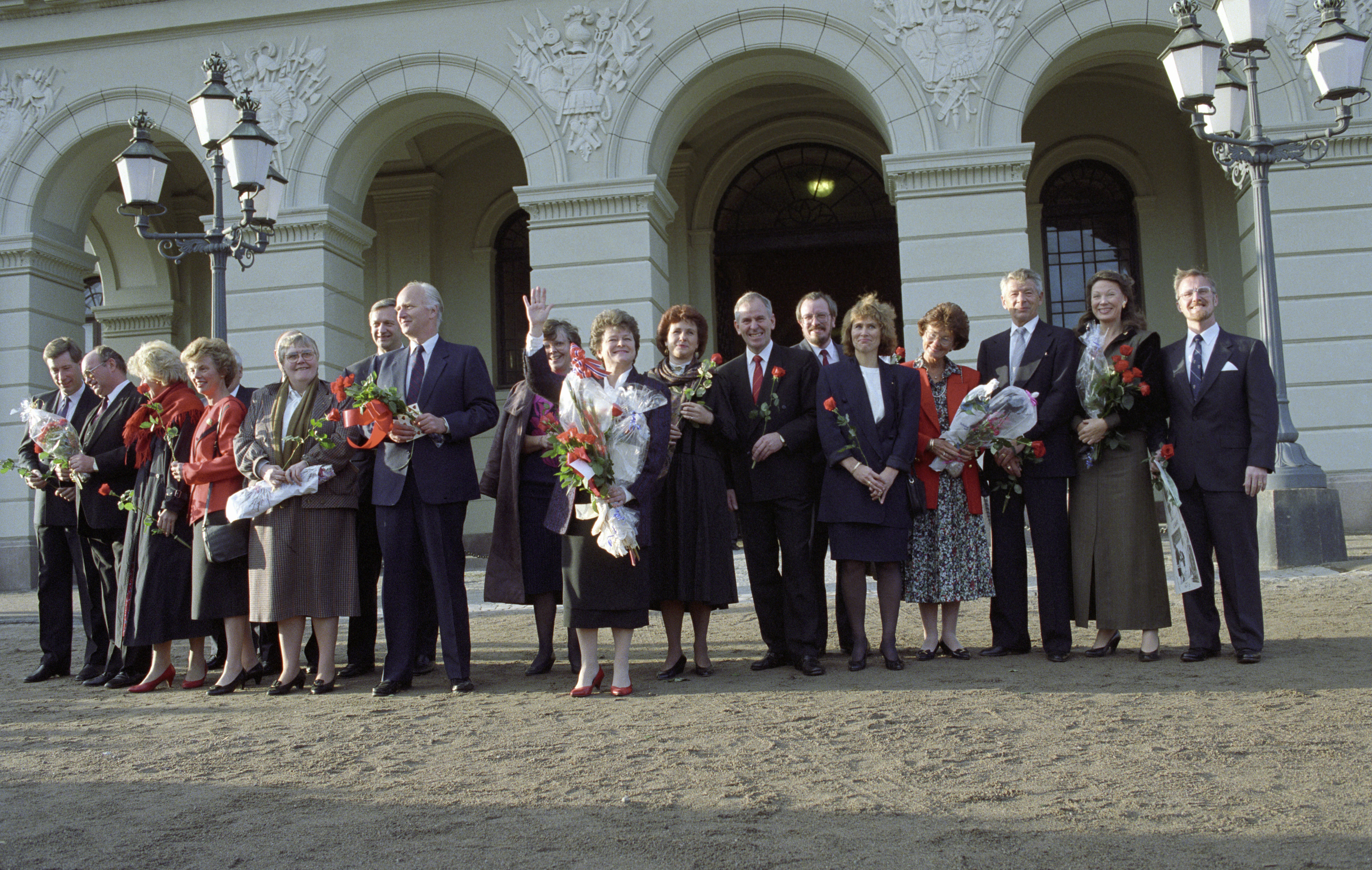 Gro Harlem Brundtlands tredje regjering foran slottet i 1993. Regjeringsmedlemmene ser ut mot folket i retning kamera, Brundtland holder blomsterbukett og vinker.