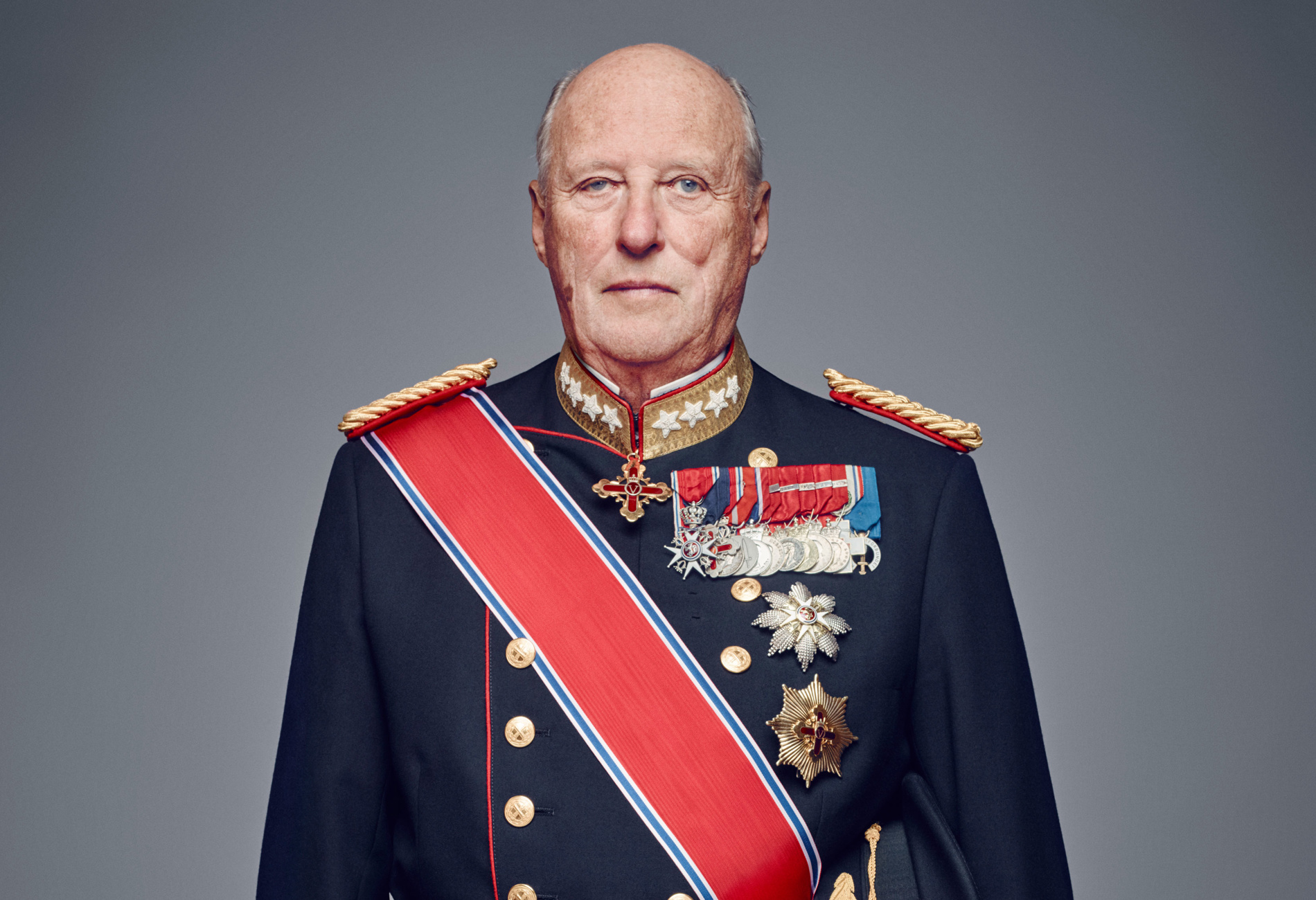 Portrettbilde av Kong Harald V. Han har på en blå uniform smykket med medaljer. 