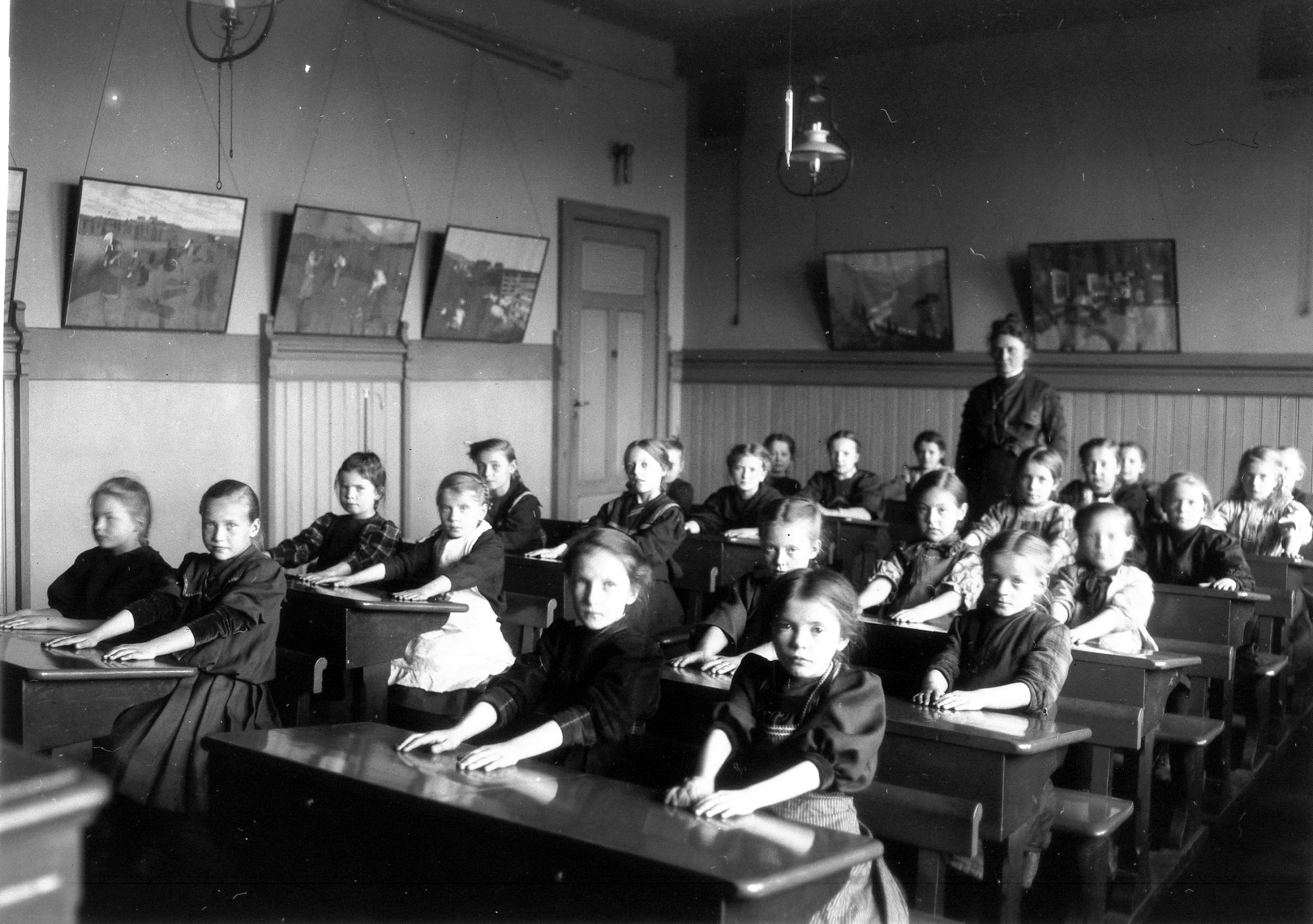 Svart hvitt bilde av en skoleklasse. Læreren står bakerst i klassen.