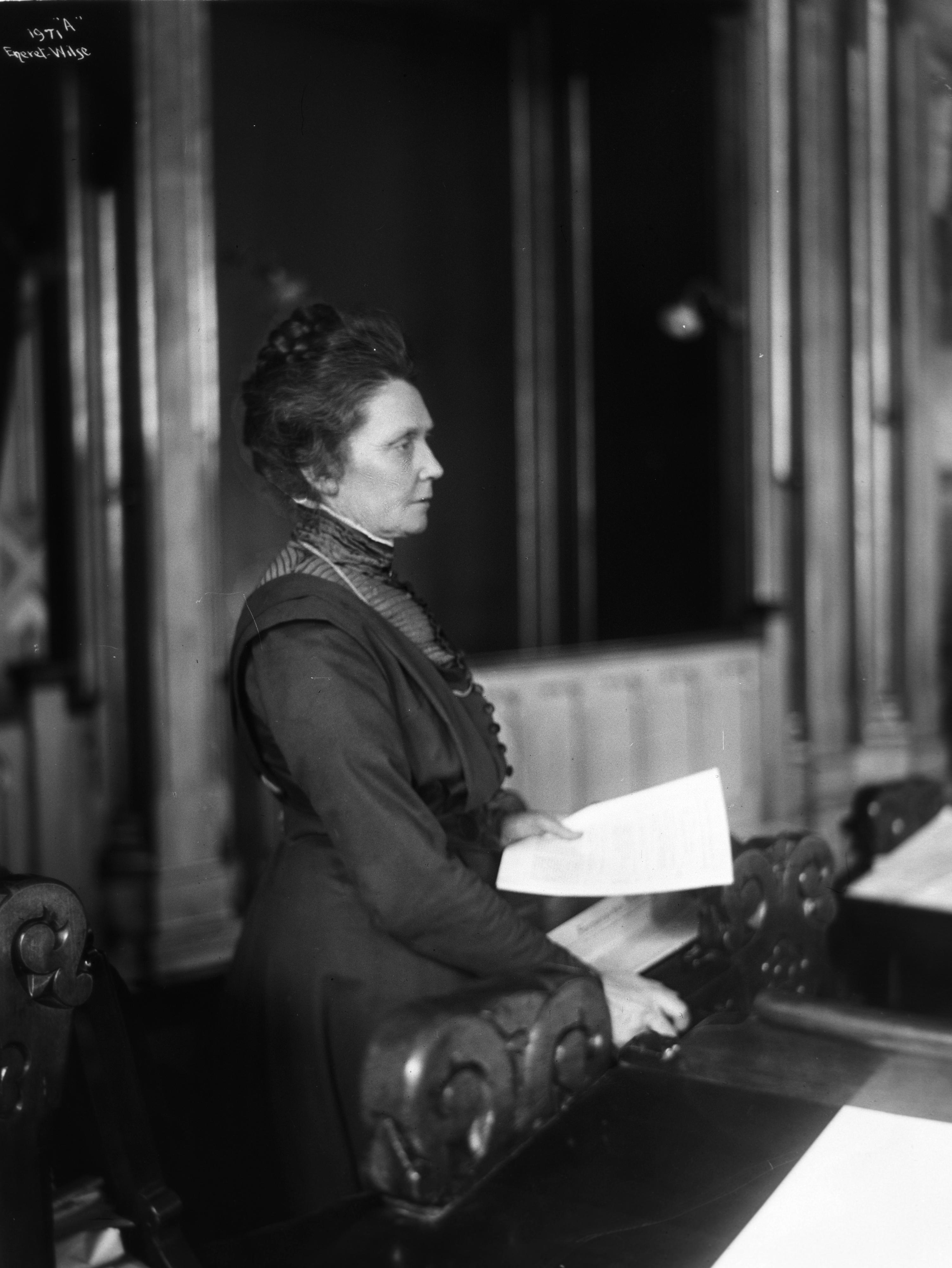 En kvinne står med et papir i hånden. Bildet er i svart hvitt.