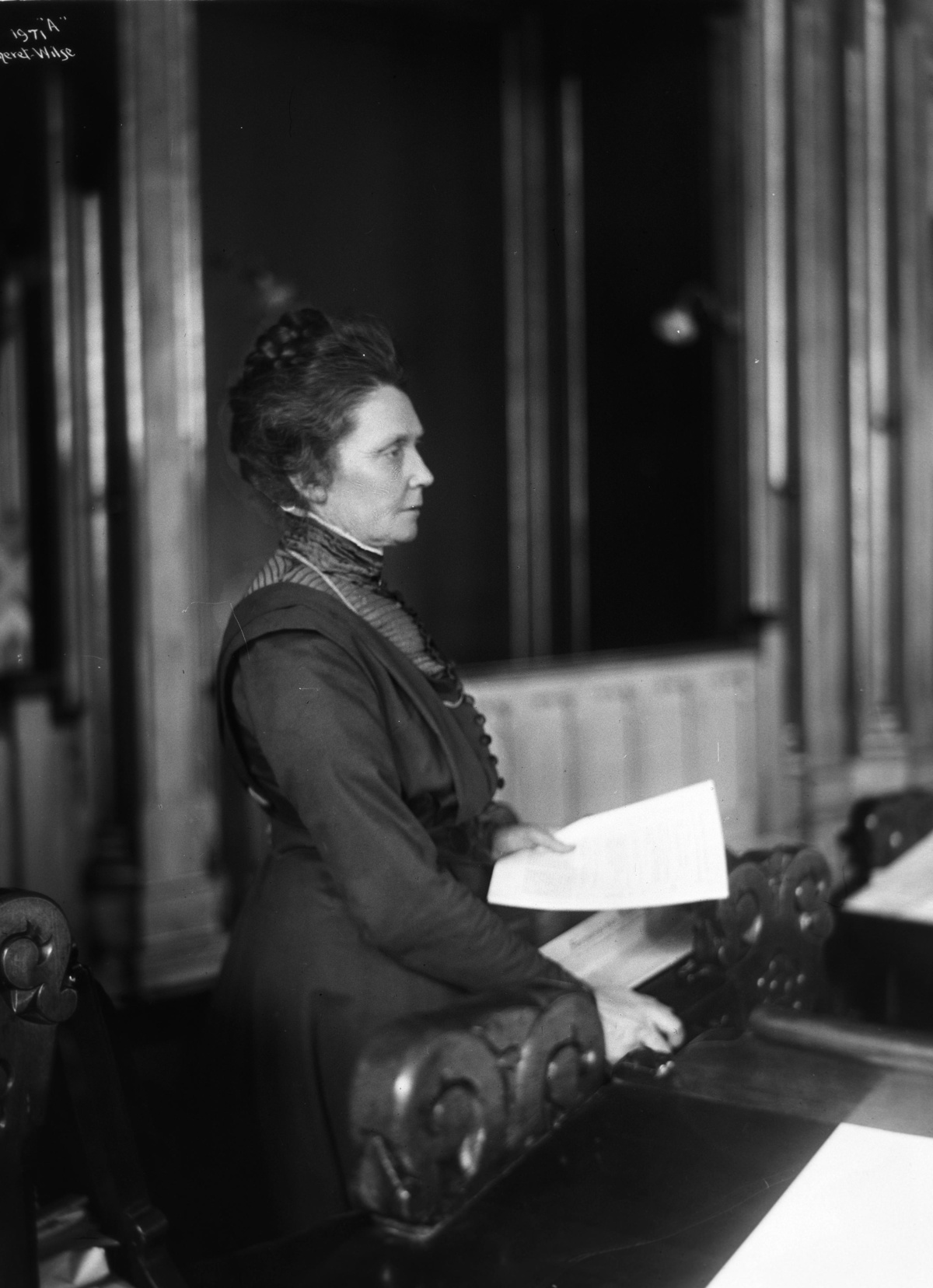 En kvinne står med et papir i hånden. Bildet er i svart hvitt.