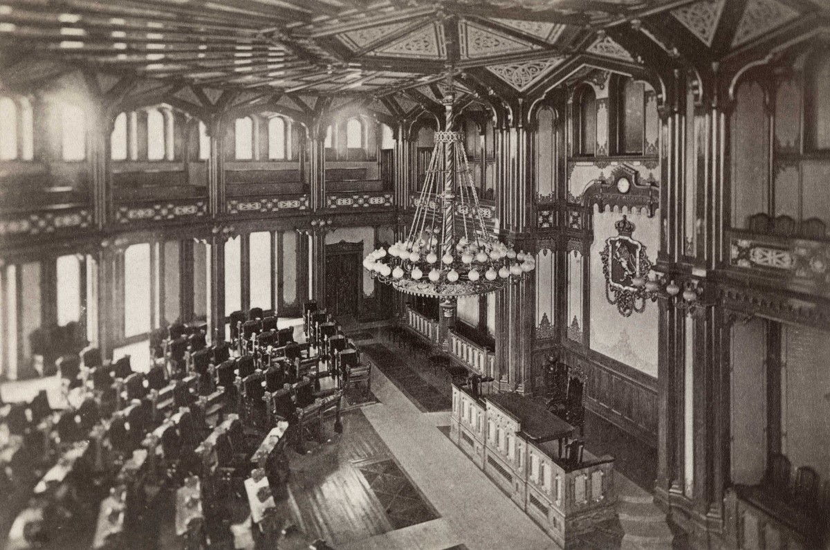 Stortingssalen ca. 1870. Veggene er hvite, og et stort riksvåpen henger der maleriet Eidsvold 1814 henger i dag.