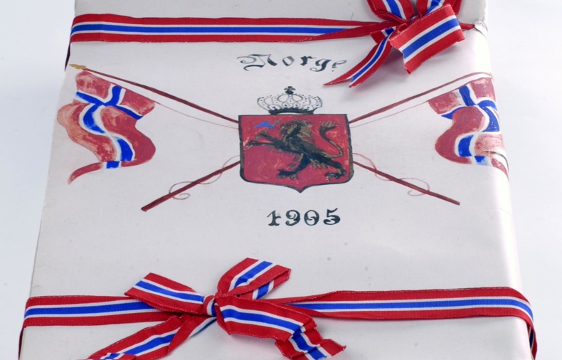 En mappe med ark inni, dekket med bånd i fargene rødt, hvitt og blått. Foran er det tegnet inn riksvåpenet, og det står "1905"