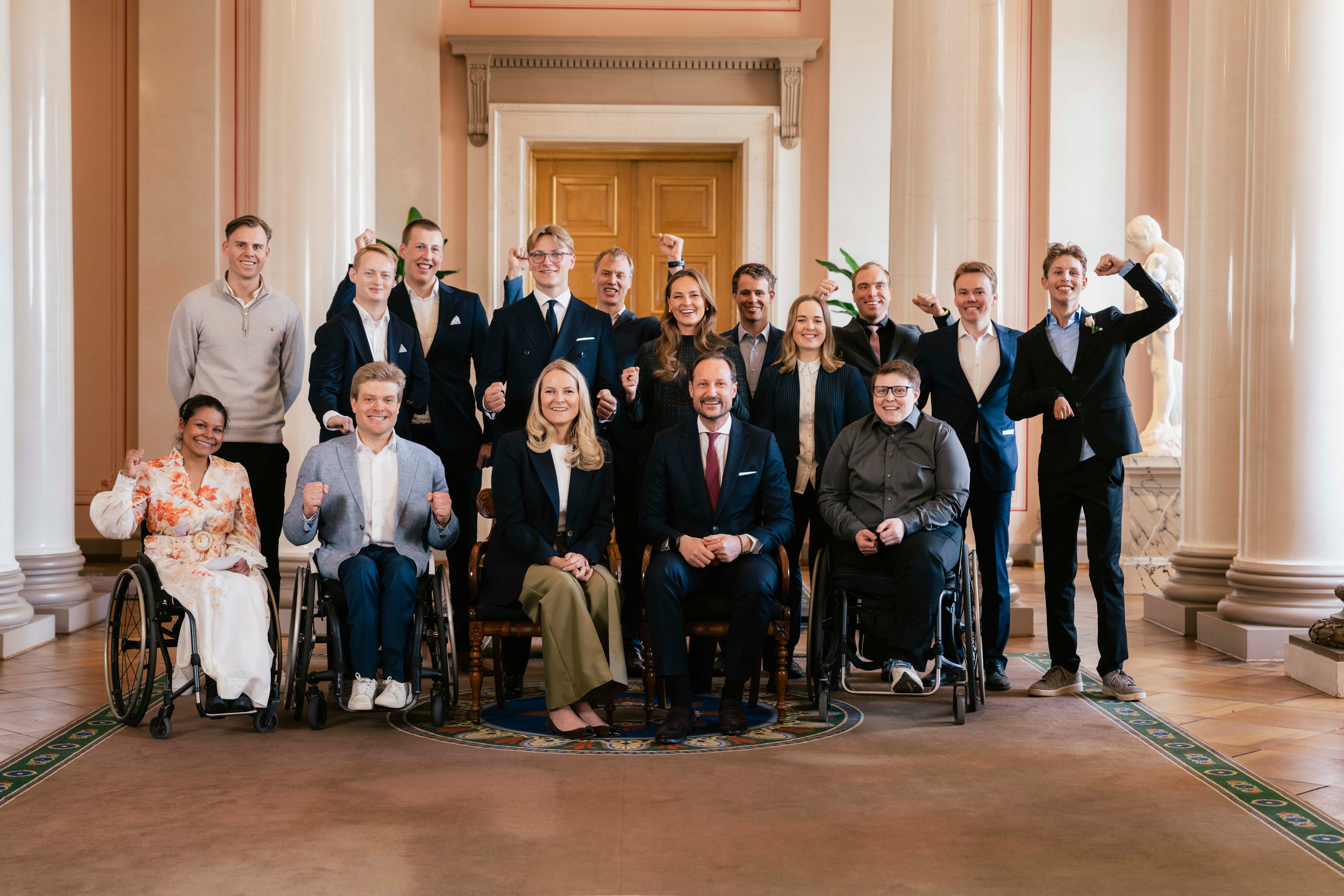 Daværende kronprins Haakon og kronprinsesse Mette Marit på slottet. Rundt dem står utøvere fra Paralympics i 2026.