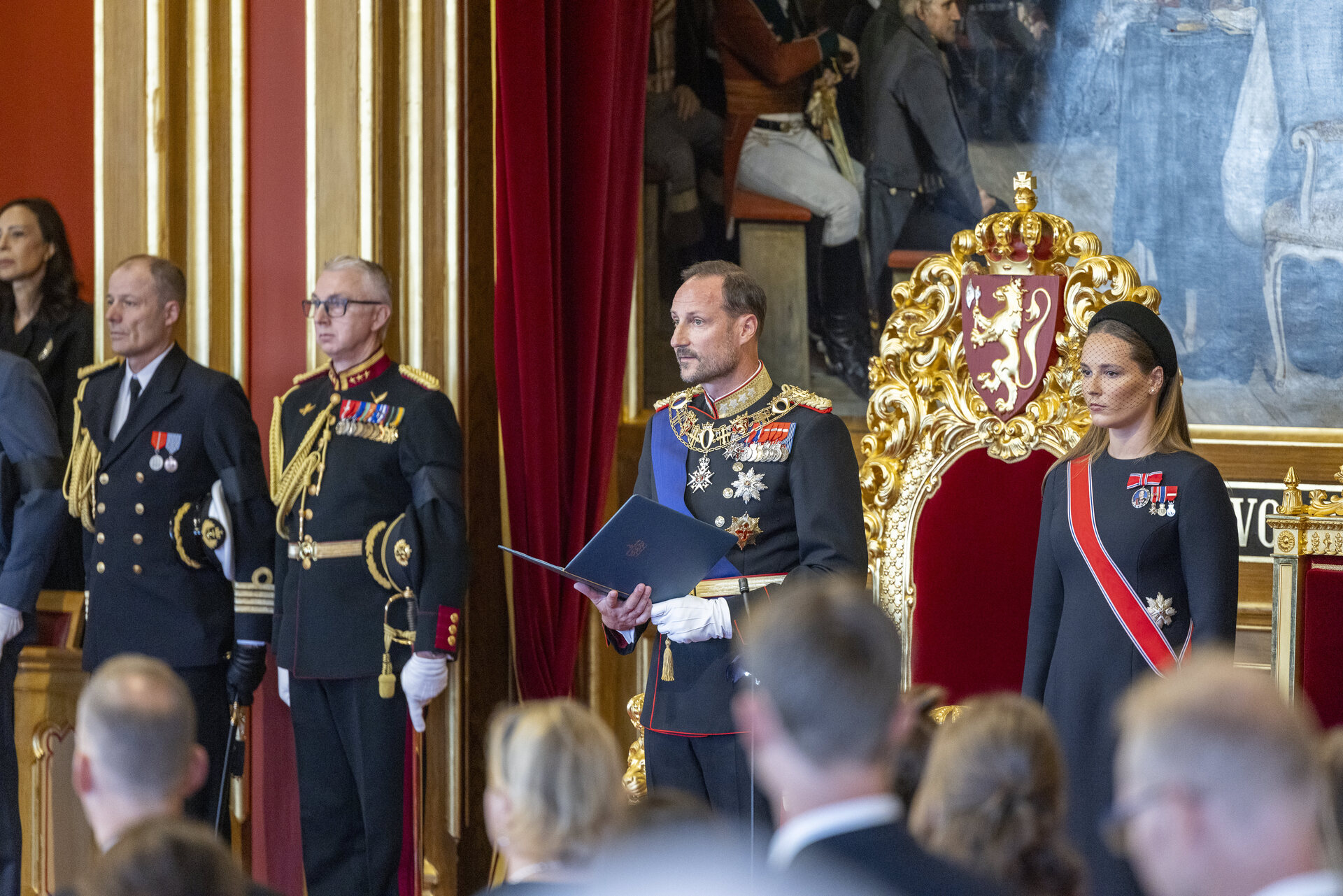 Edsavleggelse i stortingssalen. Kong Haakon VIII står foran tronstolen og leser eden til Grunnloven. Kronprinsesse Ingrid Alexandra står ved siden av. 