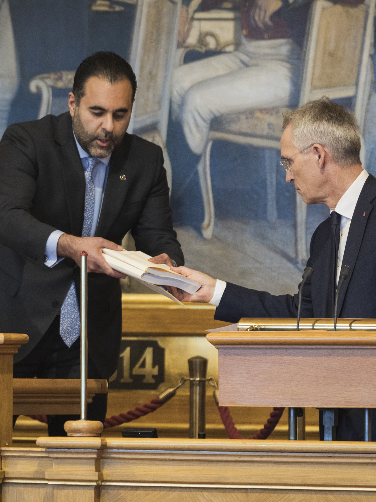 Jens Stoltenberg gir to bøker til stortingspresidenten i stortingssalen.
