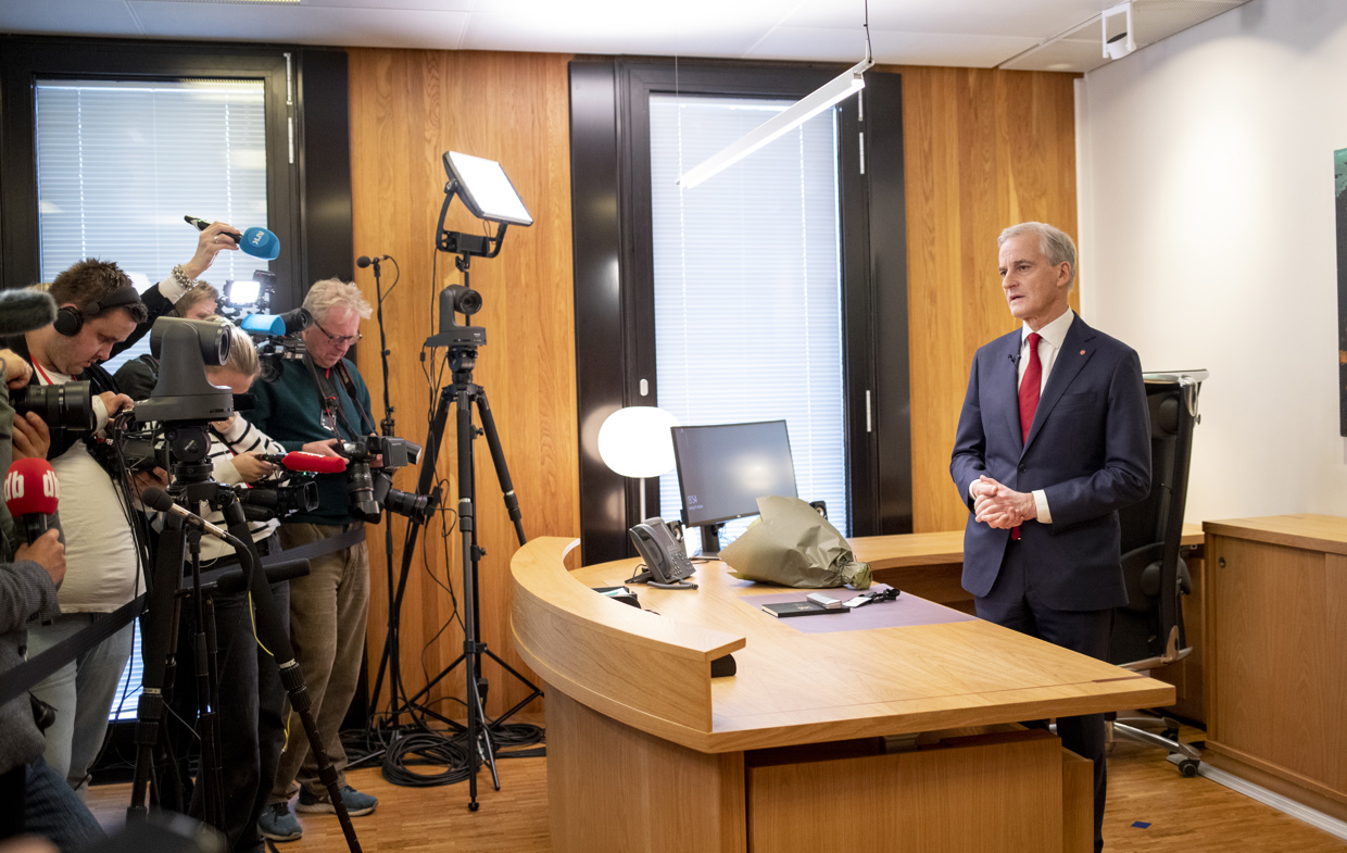 Jonas Gahr Støre står bak skrivebordet på sitt kontor. Ovenfor han står det pressefolk med mikrofoner og kameraer.