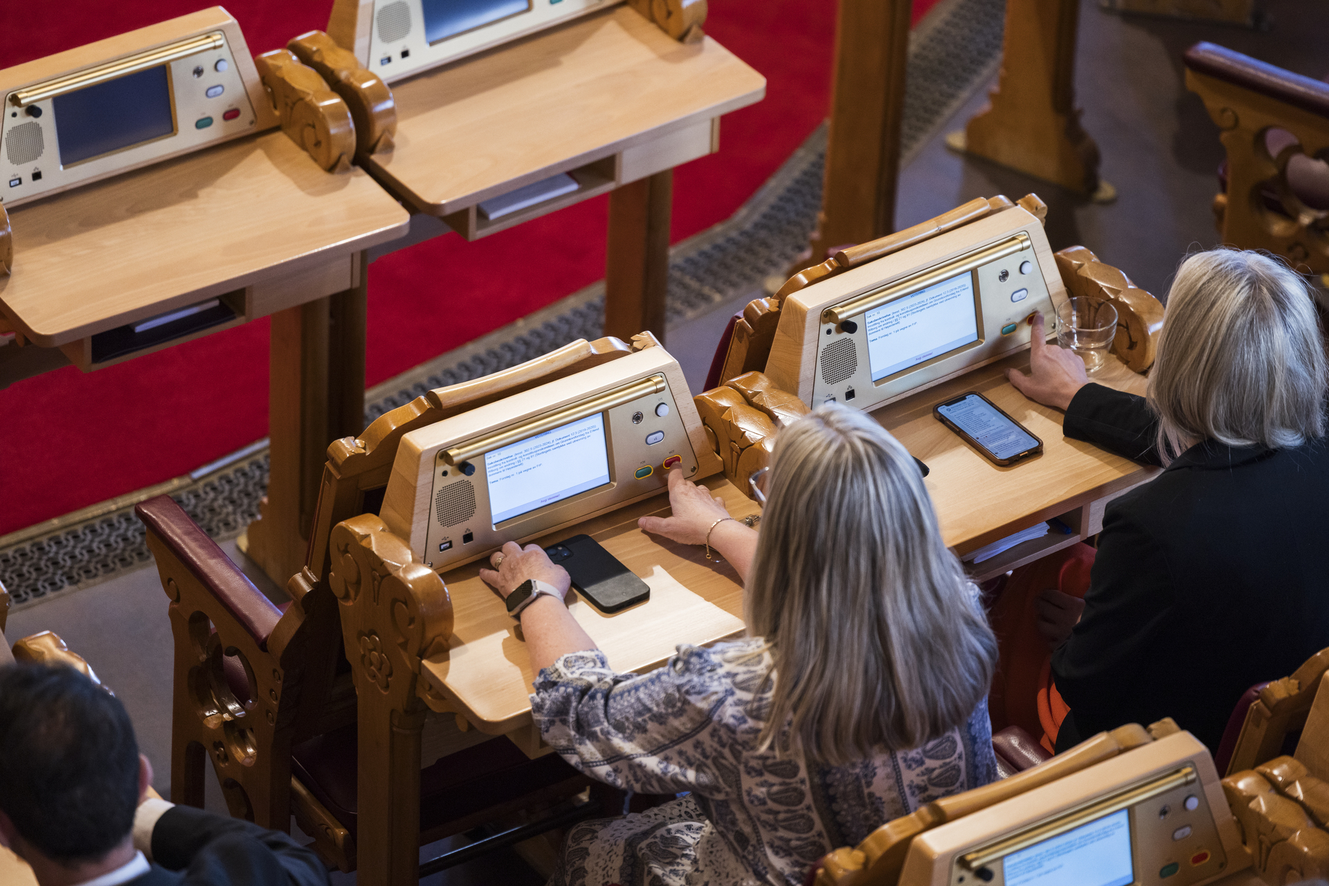 Stortingssaleb. To representanter sitter med ryggen til. De trykker begge på mot-knappen på voteringspanelet.