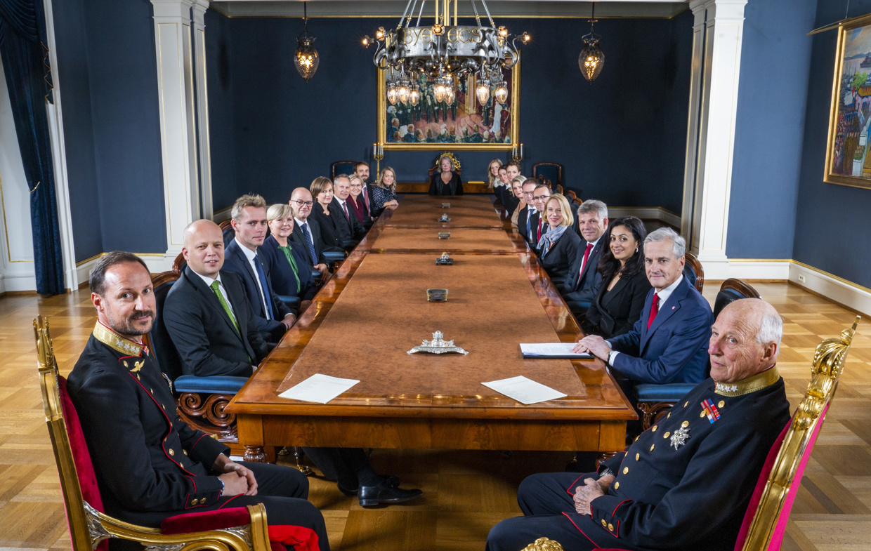 Kong Harald, Kronprins Haakon og regjeringen sitter rundt et bord.
