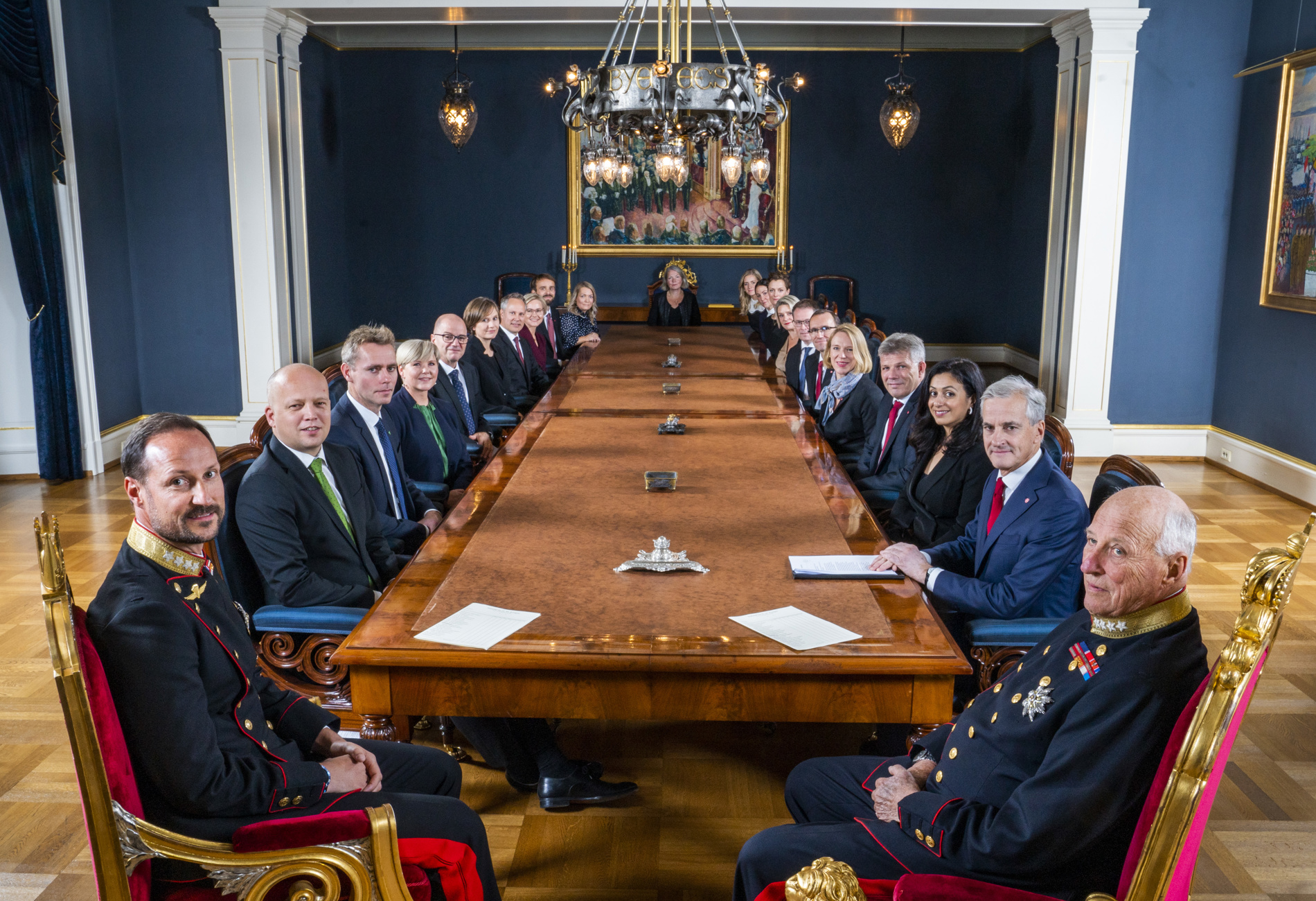 Kong Harald, Kronprins Haakon og regjeringen sitter rundt et bord.