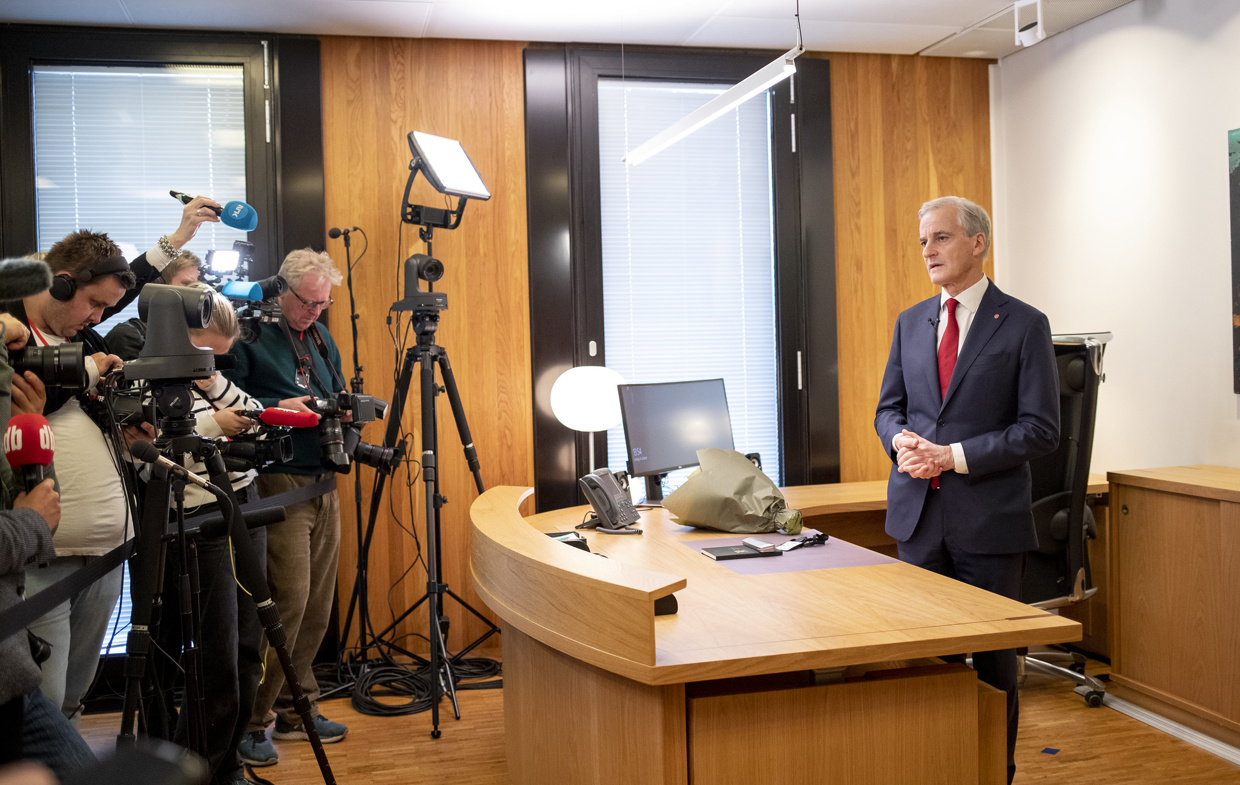 En mann står bak en pult. Mange fotografer og journalister står på siden.