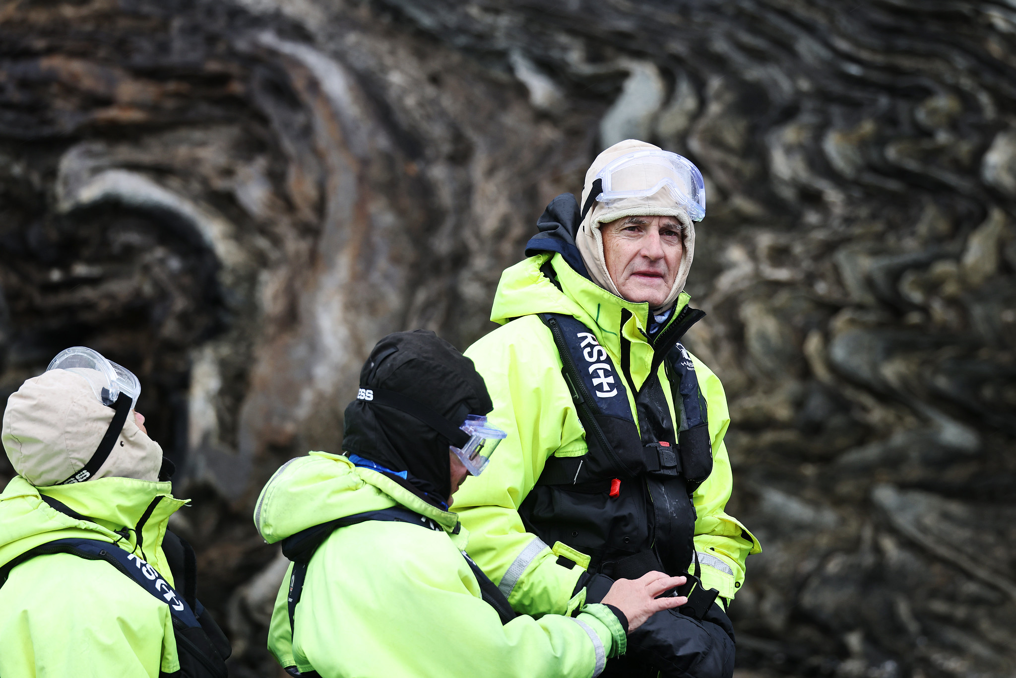 Tre mennesker i gule jakker, hetter og briller.