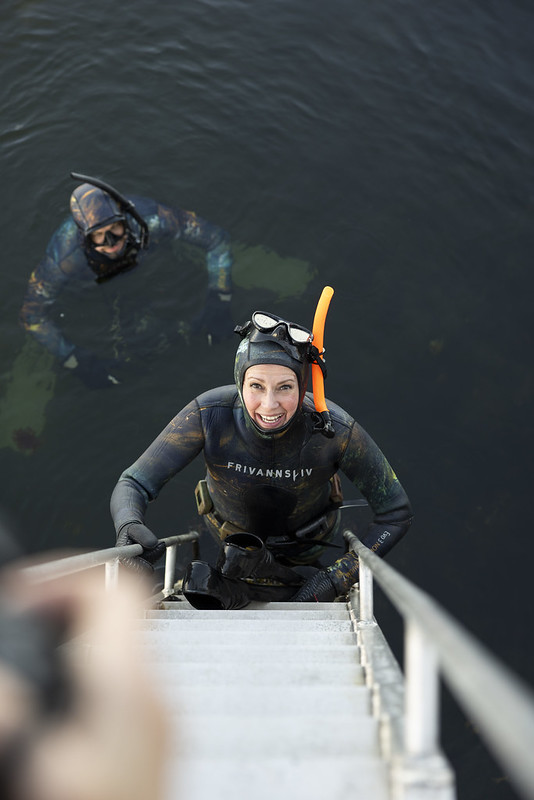 En kvinne er på vei opp av havet i dykkerdrakt.
