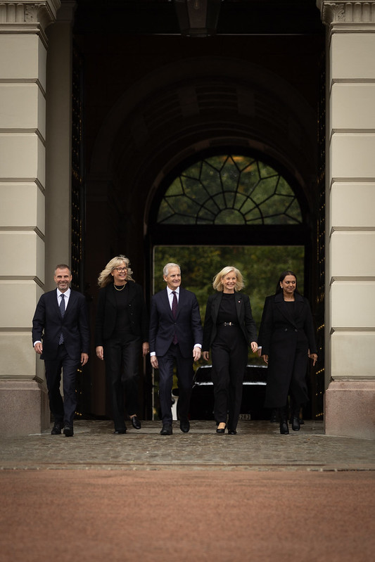 Fem mennesker kommer gående ut på slottsplassen fra slottet. Statsministeren går i midten. 