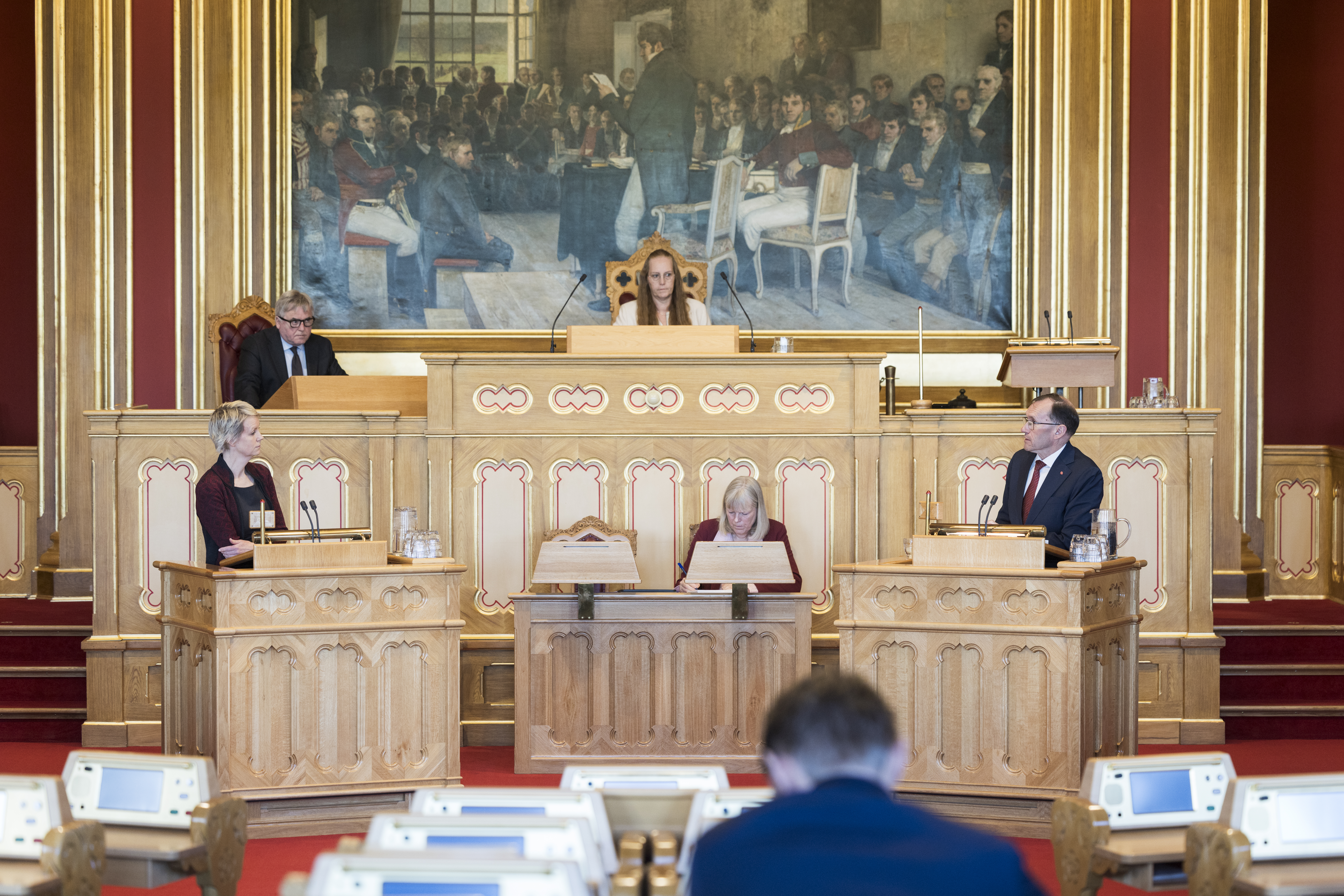Stortingssalen. To politikere står på hver sin talerstol. Stortingspresidenten sitter i midten under Eidsvold 1814-maleriet.