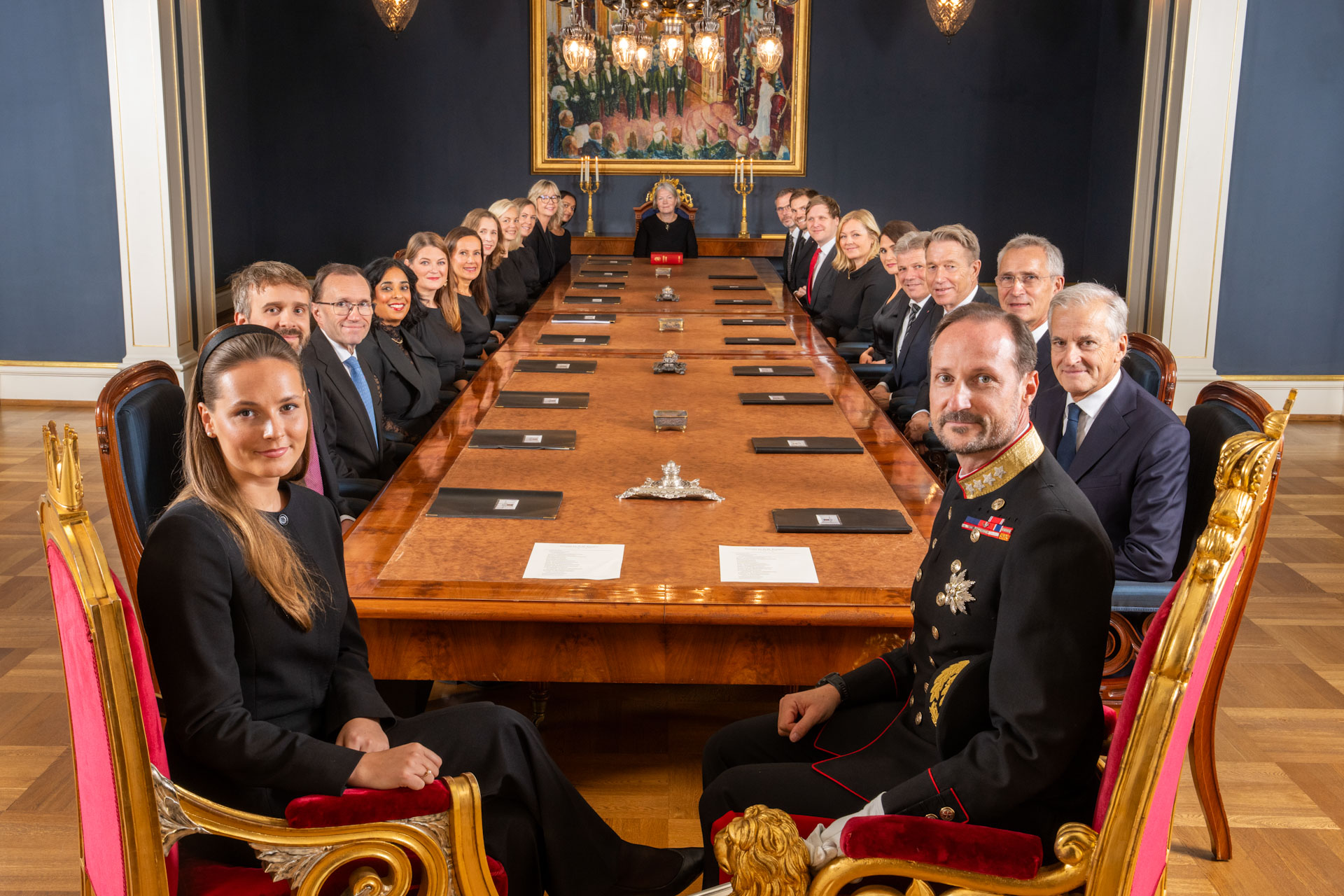 Kongen i statsråd på slottet. Kong Haakon VIII og kronprinsessen sitter ved enden av bordet. Langs langsidene sitter statsministeren og hans regjering. 