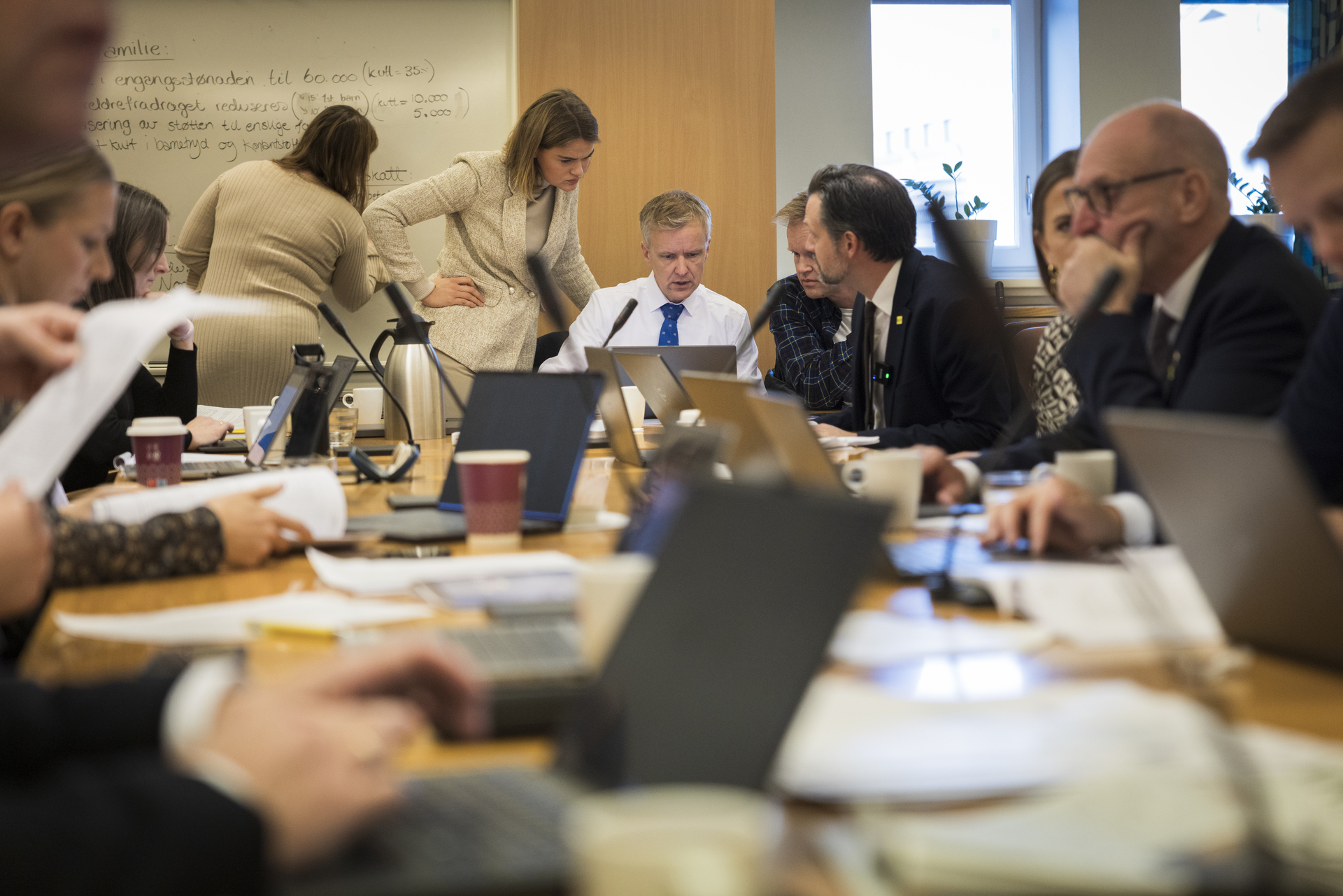 Mange mennesker sitter rundt et bord med datamaskiner og papirer.