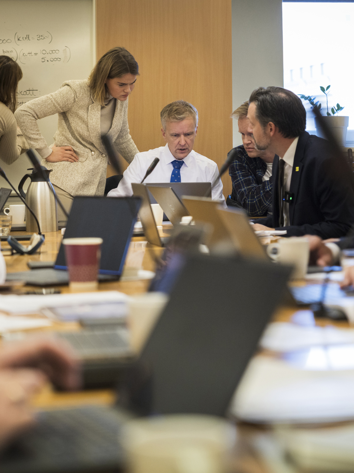 Mange mennesker sitter rundt et bord med datamaskiner og papirer.