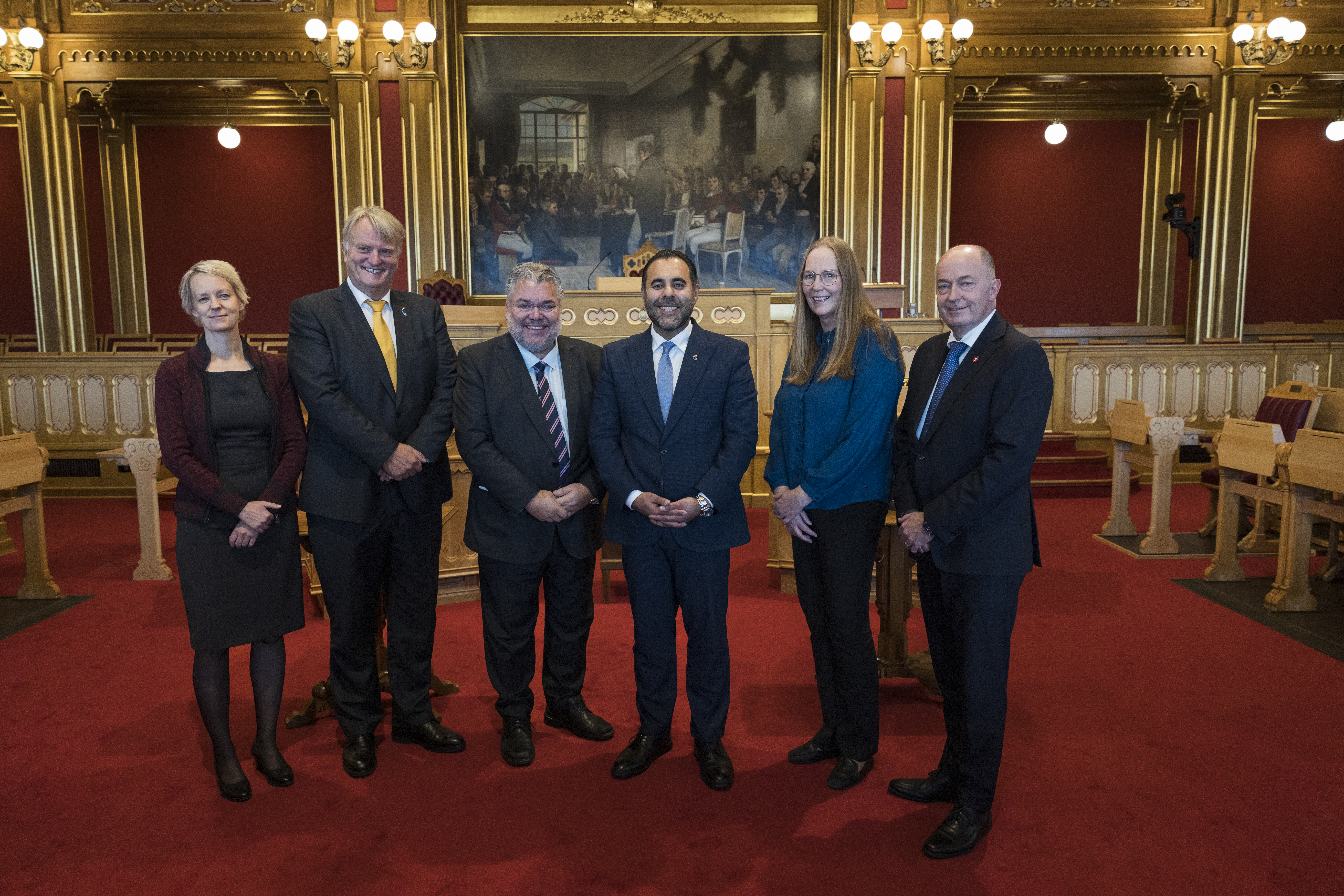 Seks personer står ved siden av hverandre i stortingssalen.