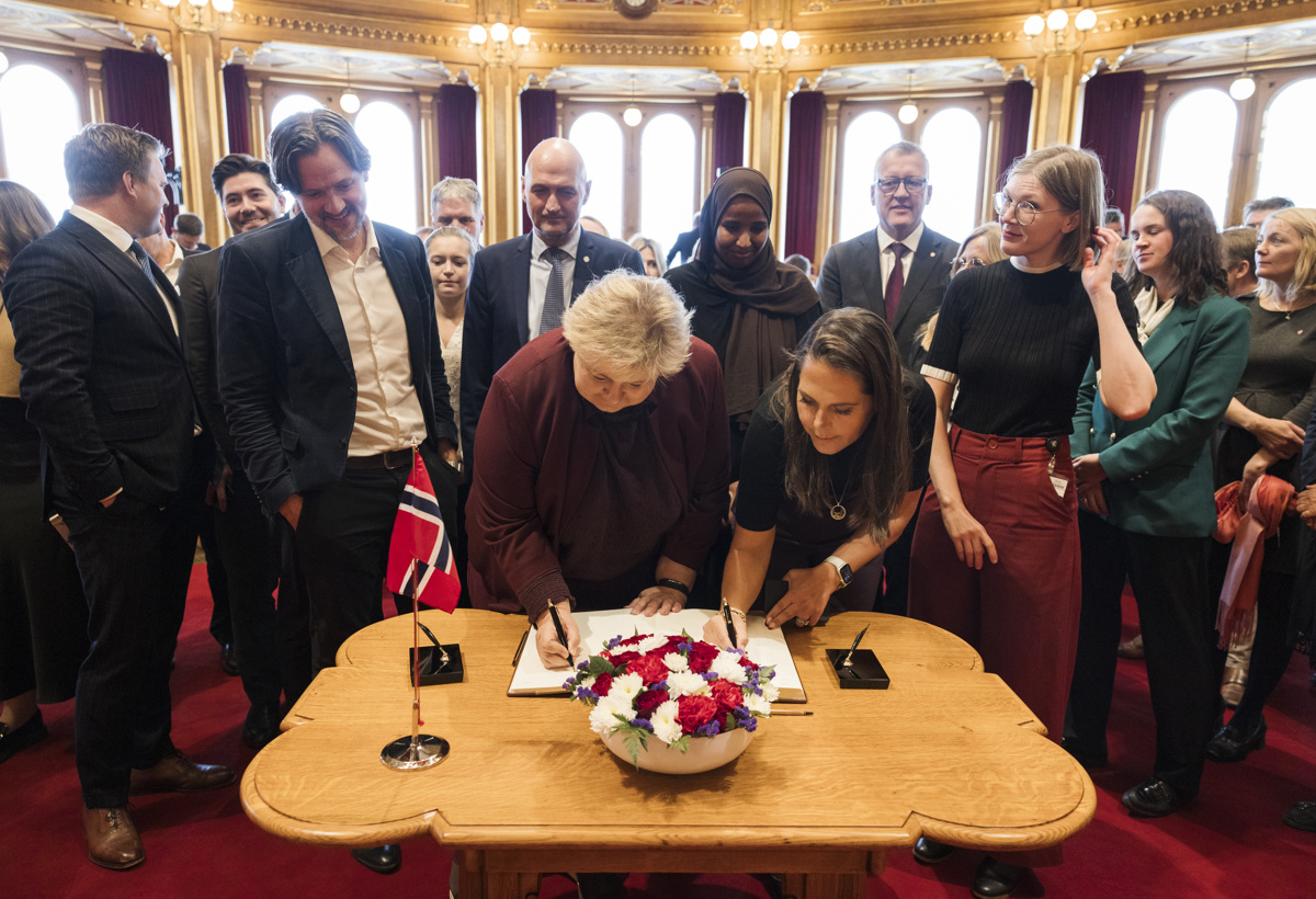 Mange stortingsrepresentanter står rundt et bord og venter på å signere.