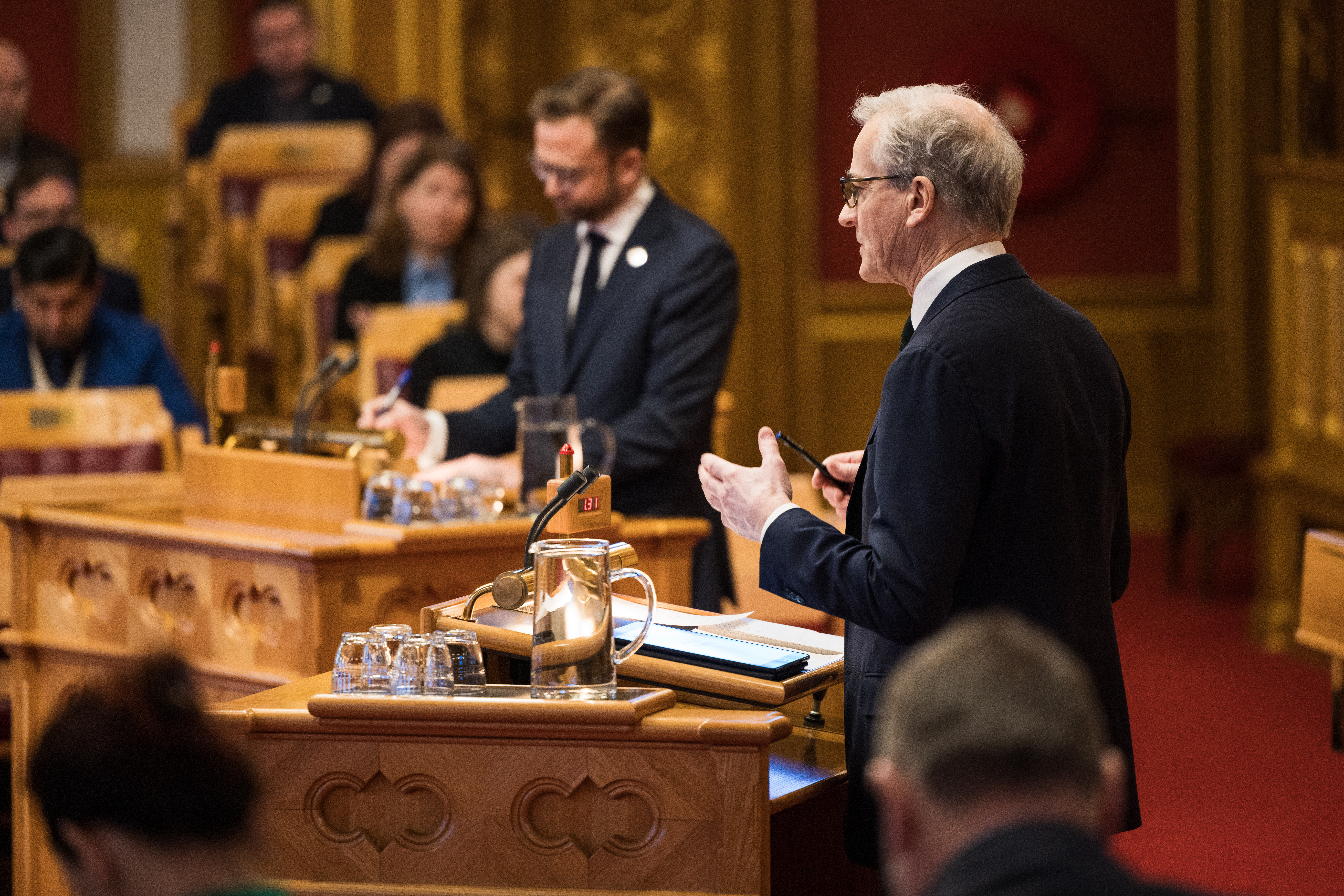 Jonas Gahr Støre sett bakfra på Stortingets talerstol, der han svarer på spørsmål fra Nikolai Astrup