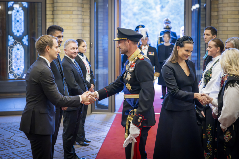 Inngangspartiet i stortingsbygningen. Kong Haakon VIII og kronprinsessen er på vei inn i Stortinget og hilser på stortingsrepresentantene som står klare for å ta dem imot. 