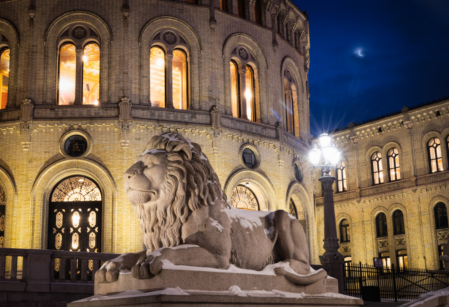 Stortingsbygningen og løven om kvelden. Månen er oppe på himmelen.