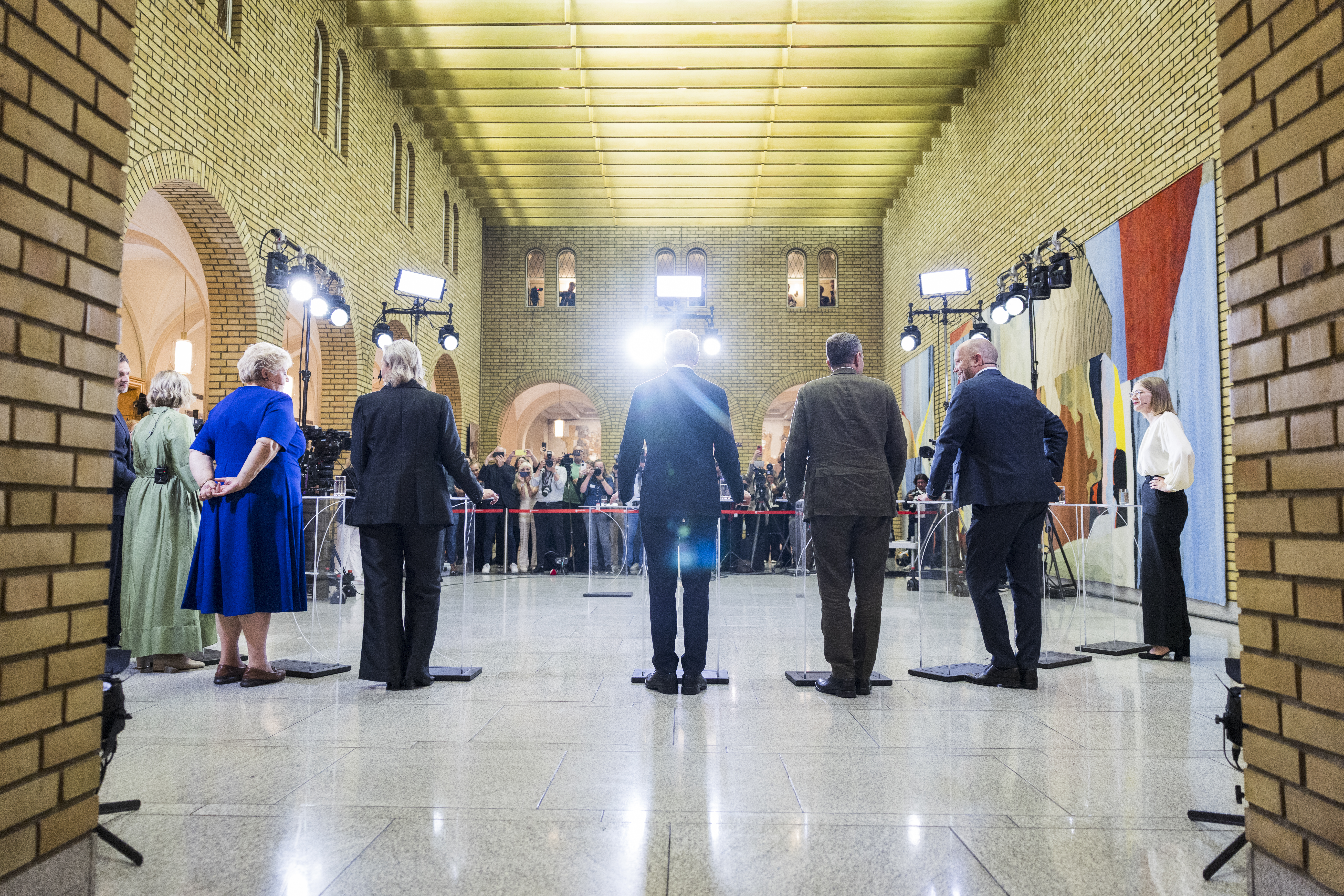 En gruppe mennesker står med ryggen til kamera i vandrehallen i Stortinget.